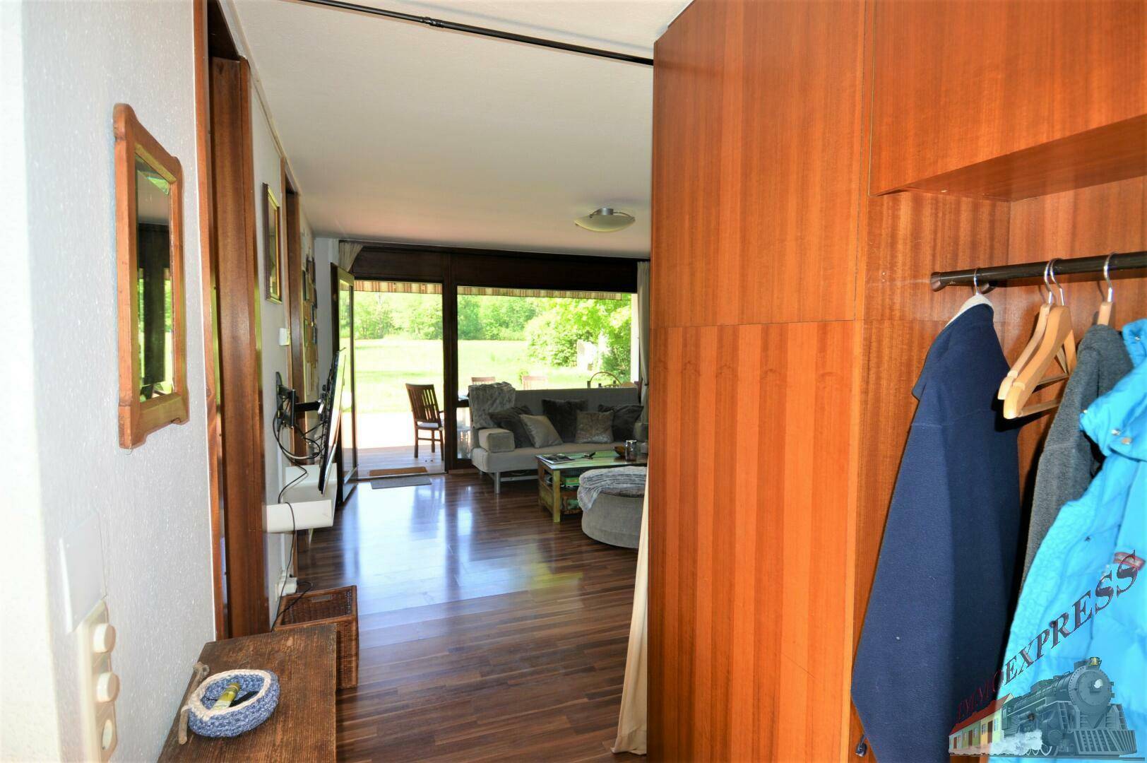 Flur mit Garderobe und Blick in den hellen Wohnbereich mit großen Fenstern.