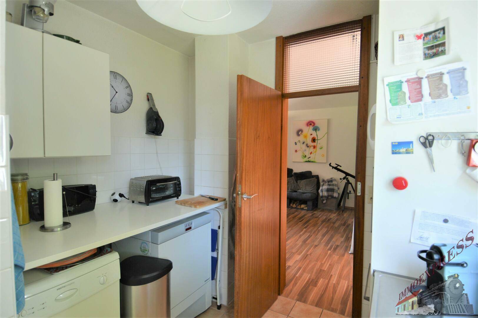 Kleine Küche mit weißen Schränken, Arbeitsplatte und Blick in den Wohnbereich.
