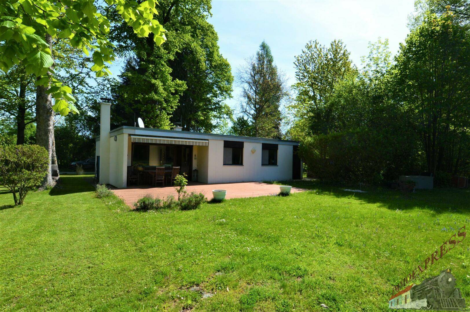 Rückansicht eines Hauses mit großer Terrasse, Esstisch im Freien und weitläufigem grünen Rasen.