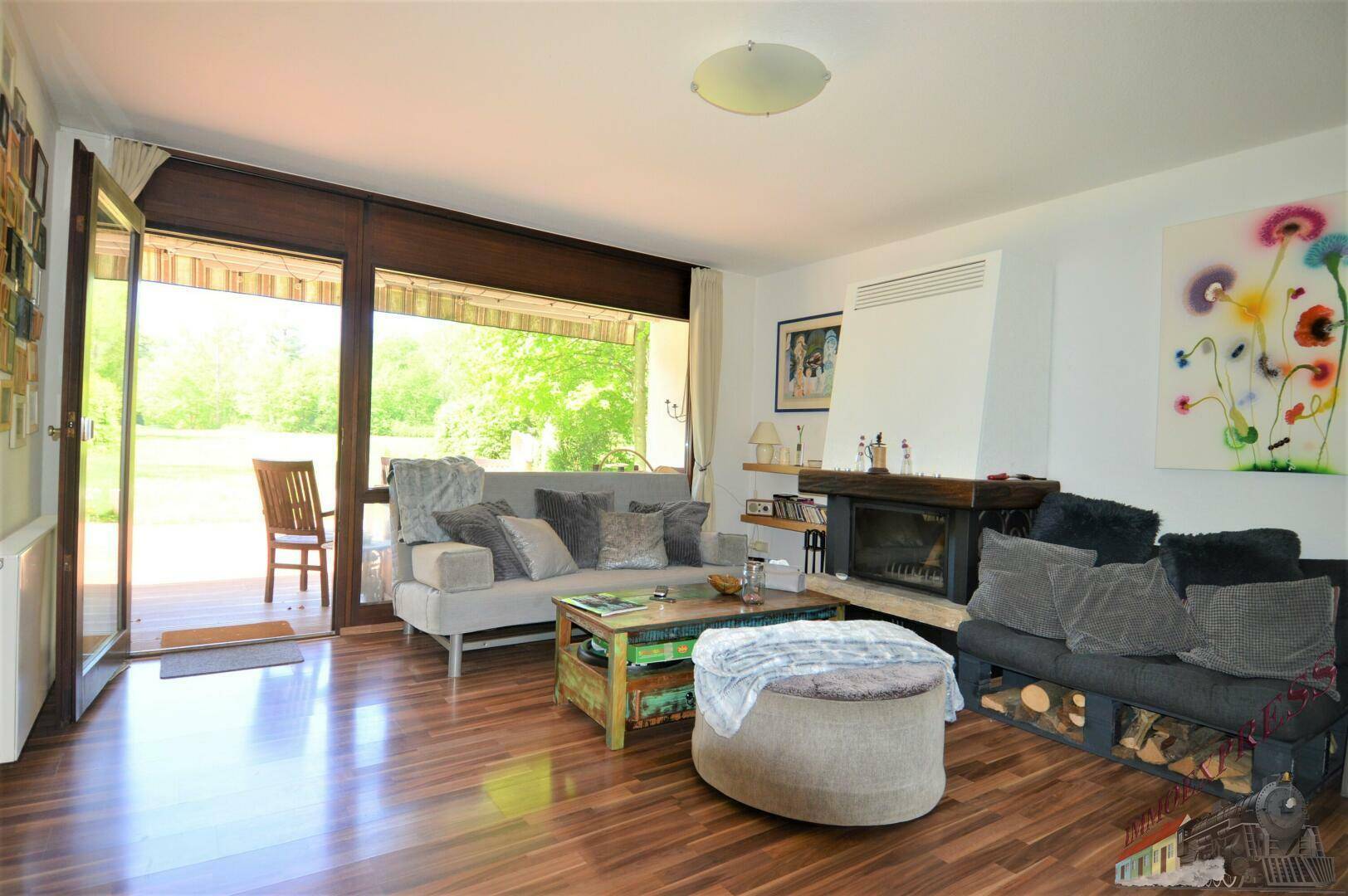 Gemütliches Wohnzimmer mit Kamin, Holzboden und Zugang zur Terrasse mit Gartenblick.