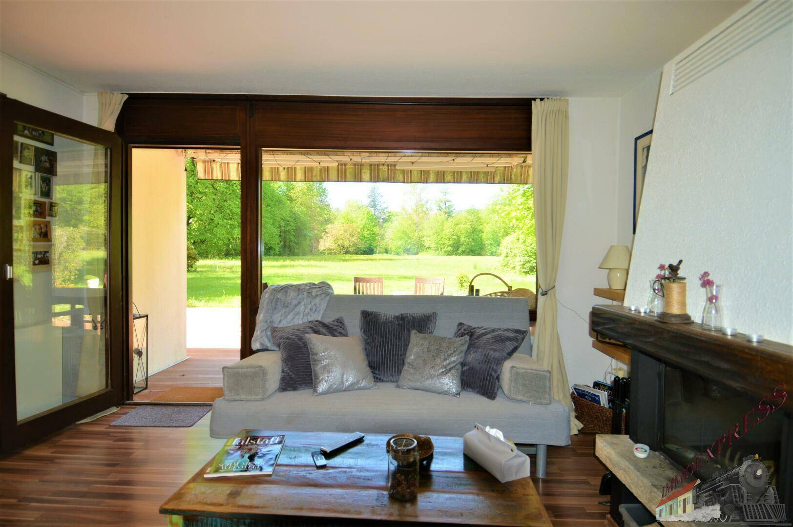 Helles Wohnzimmer mit bequemen Sofas, Kamin und großen Fenstern zum grünen Garten.
