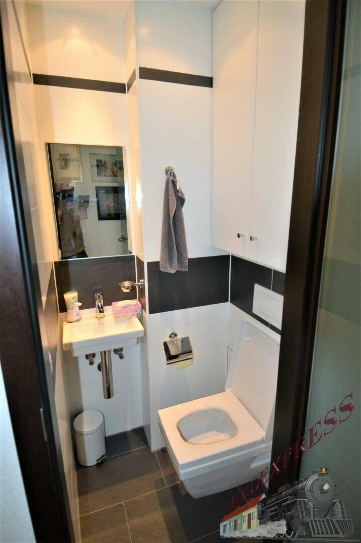 Kleines Gäste-WC mit Wand-WC, Waschbecken und Spiegel in Schwarz-Weiß-Design.