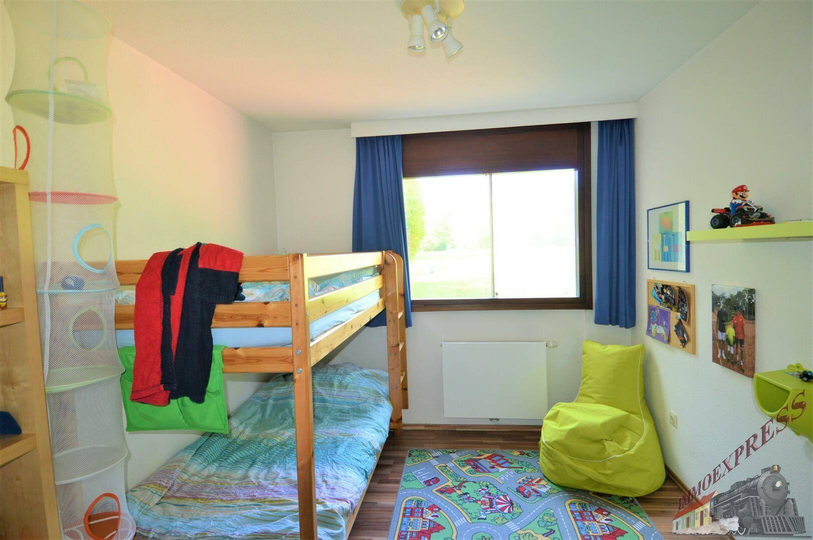 Kinderzimmer mit Etagenbett, farbenfrohem Teppich und Fenster mit Blick ins Freie.