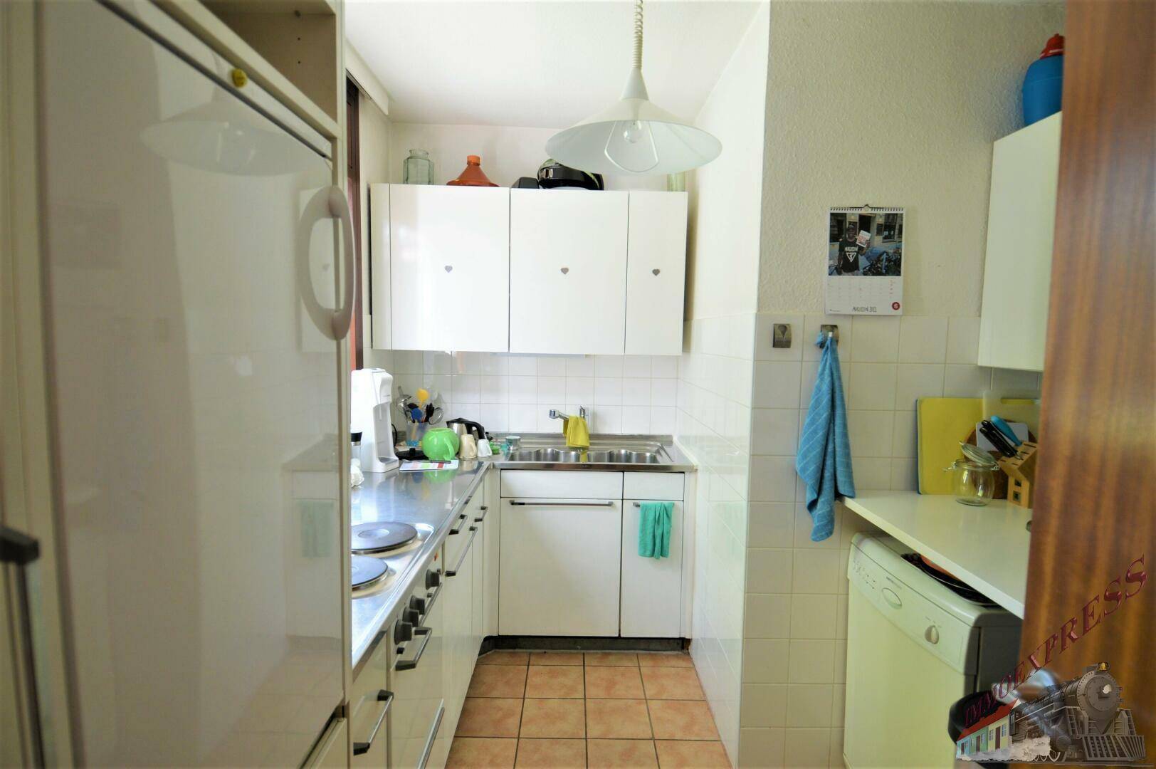 Funktionale Küche mit weißen Schränken, Edelstahlspüle und Terrakotta-Fliesenboden.