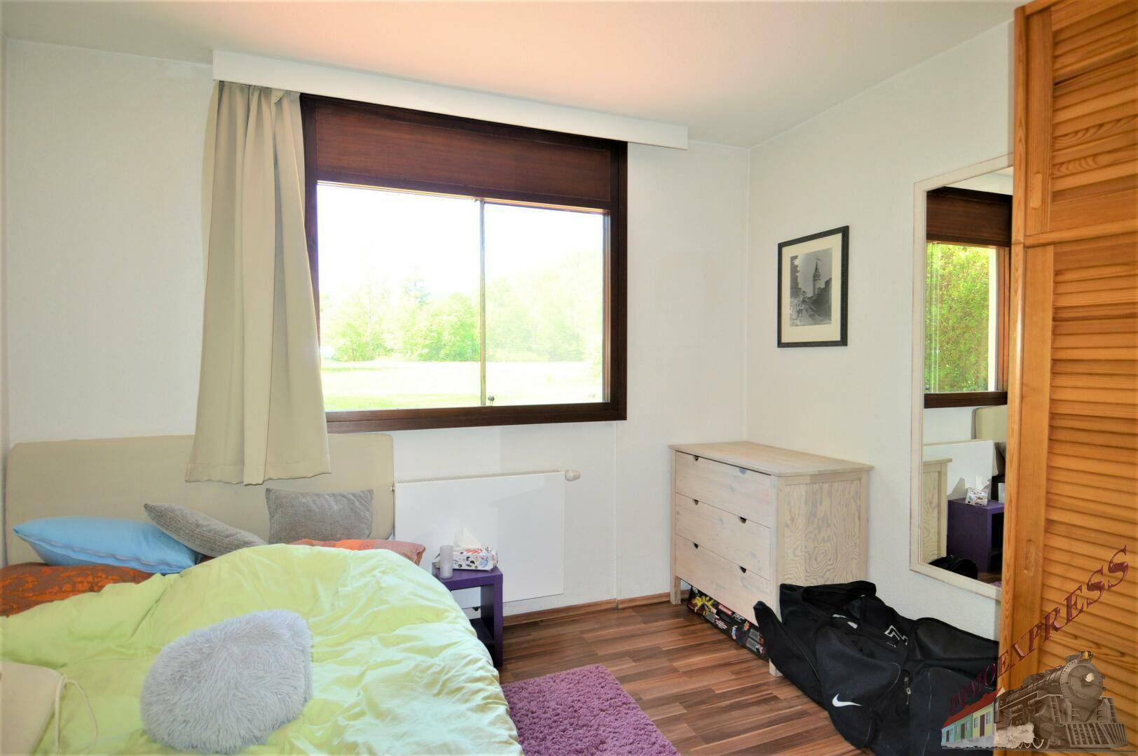 Helles Schlafzimmer mit Einzelbett, Kommode und Fenster mit Blick auf die Natur.