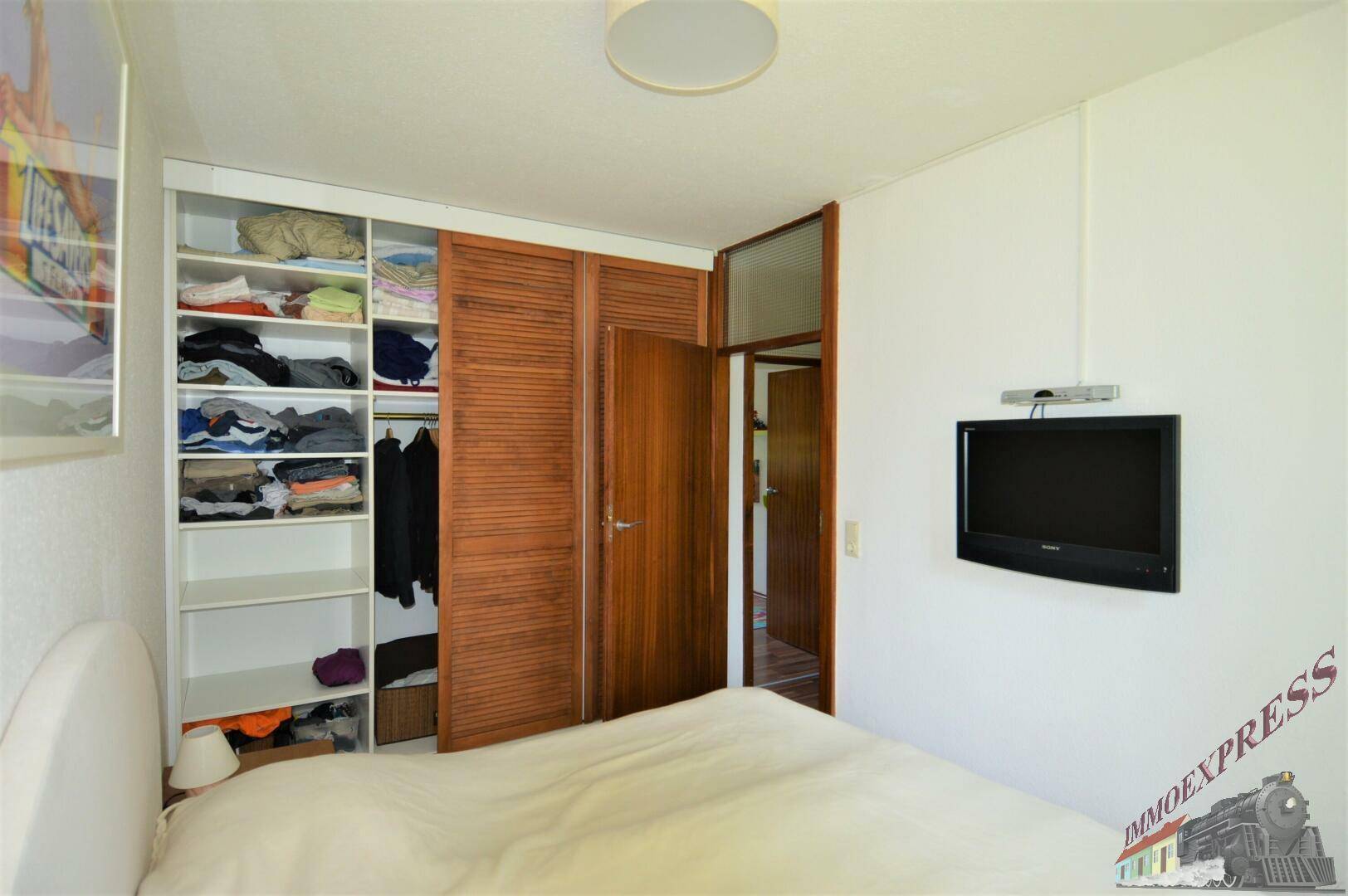 Schlafzimmer mit integriertem Kleiderschrank, Doppelbett und Zugang zu weiteren Räumen.
