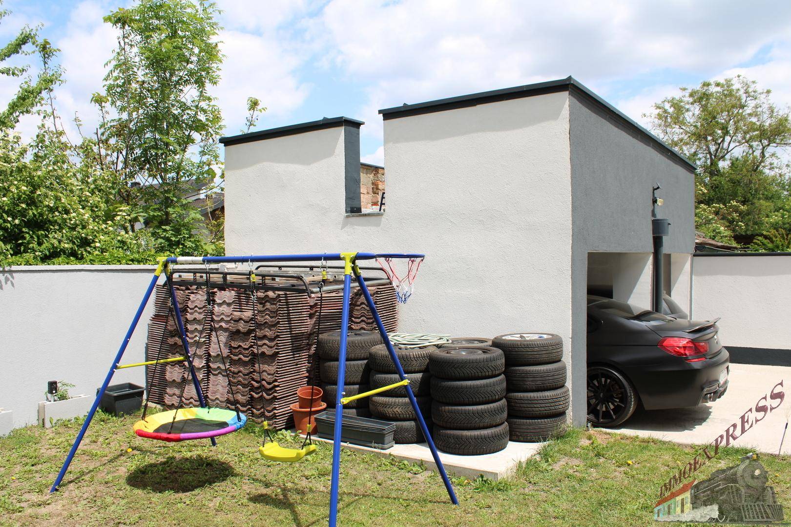 Gartenbereich mit Schaukel, Reifenstapeln und einem geparkten Auto in der offenen Garage.
