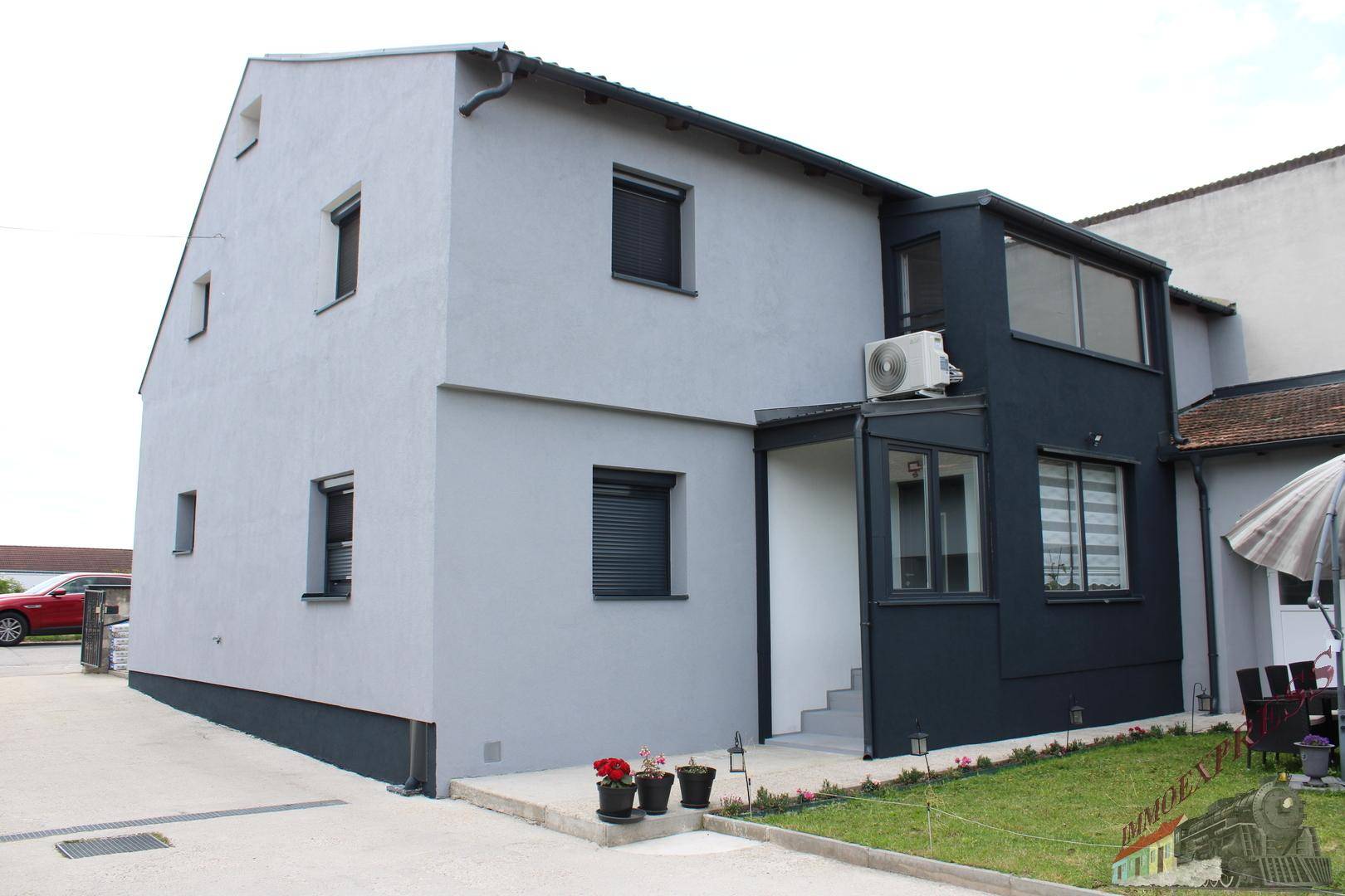 Seitenansicht des Hauses mit modernem Anbau, Klimaanlage und einem kleinen, gepflegten Rasenbereich.