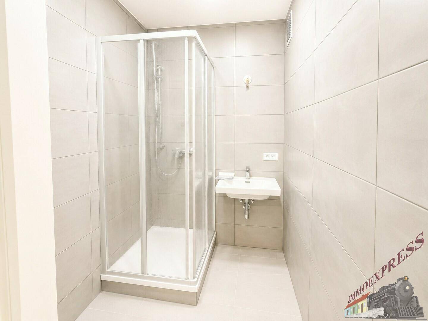 Modernes Badezimmer mit Duschkabine, Waschbecken und hellgrauen Fliesen an Wänden und Boden.