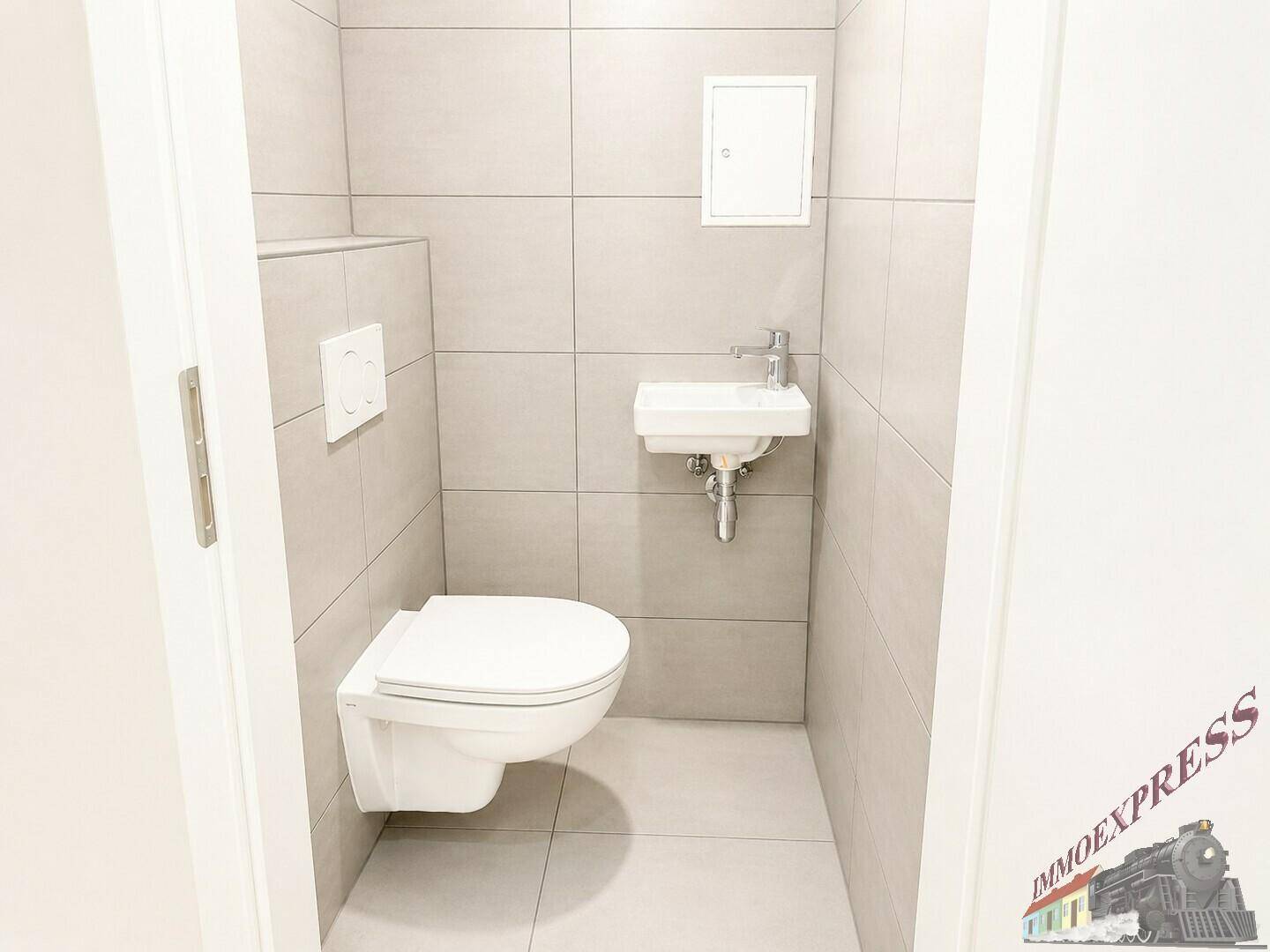 Separates WC mit wandhängender Toilette, kleinem Waschbecken und hellgrauen Fliesen.