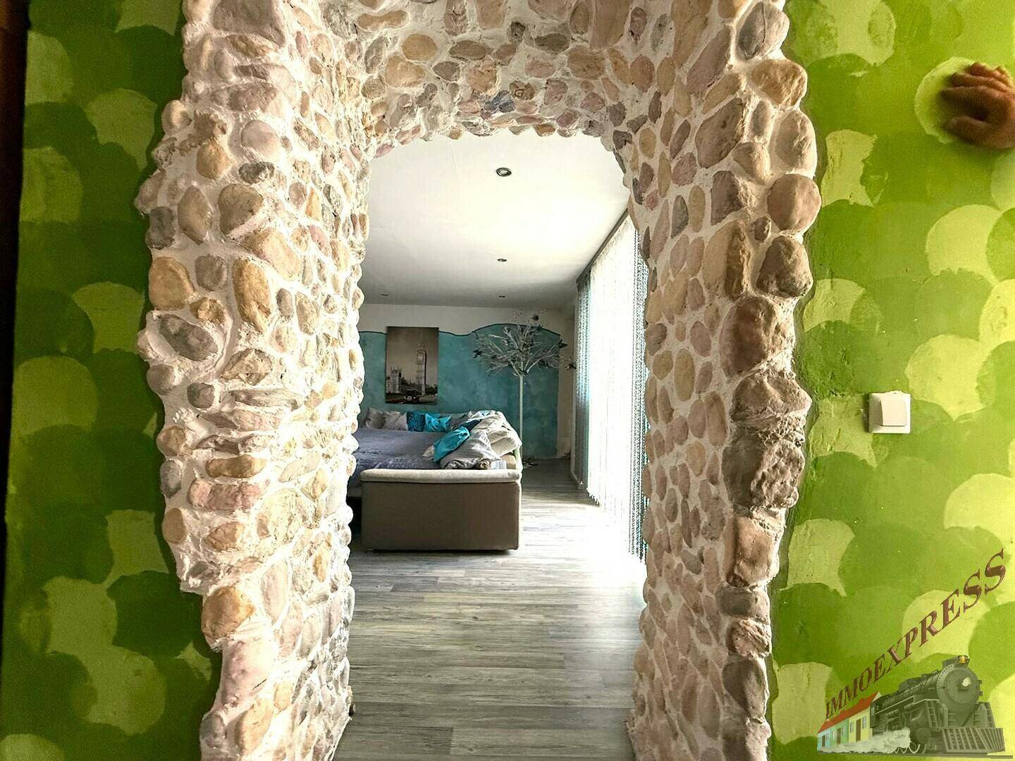 Blick durch einen rustikalen Steinbogen vom Flur in das farbenfroh gestaltete Wohnzimmer.