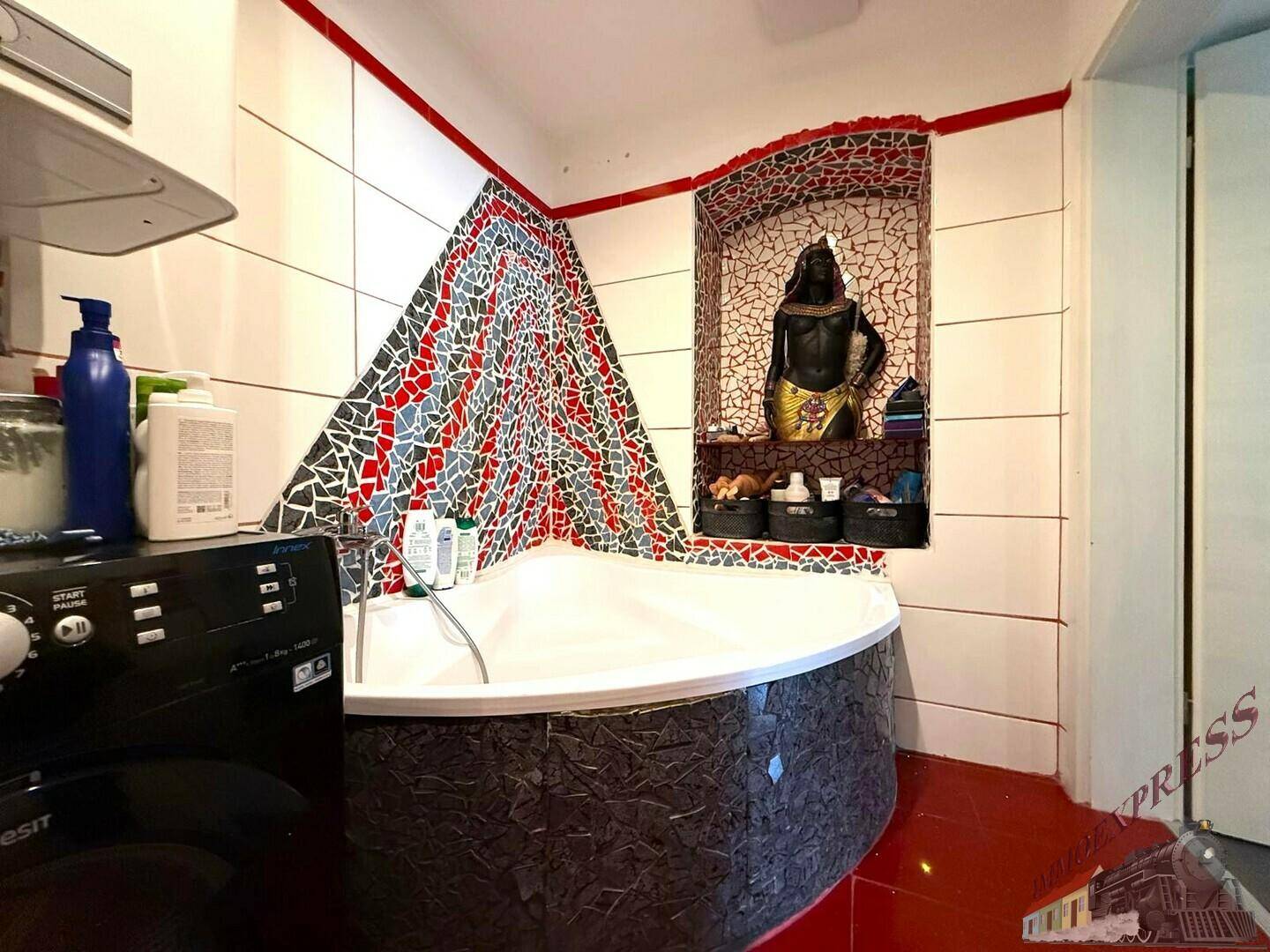 Badezimmer mit Eckbadewanne, roten Bodenfliesen und dekorativen Mosaikakzenten an den Wänden.