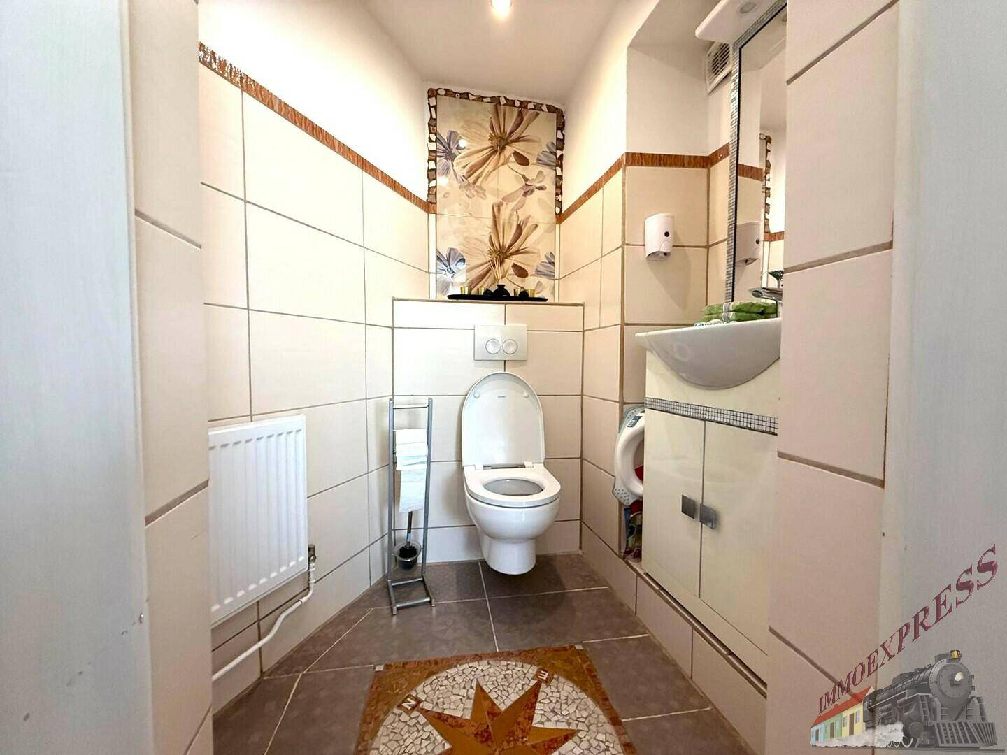 Kleines WC mit hellen Fliesen, wandhängender Toilette und einem Waschbecken.