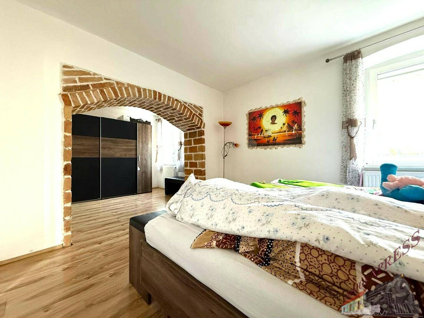 Schlafzimmer mit Laminatboden und einem dekorativen Ziegelbogen, der zu einem weiteren Bereich führt.