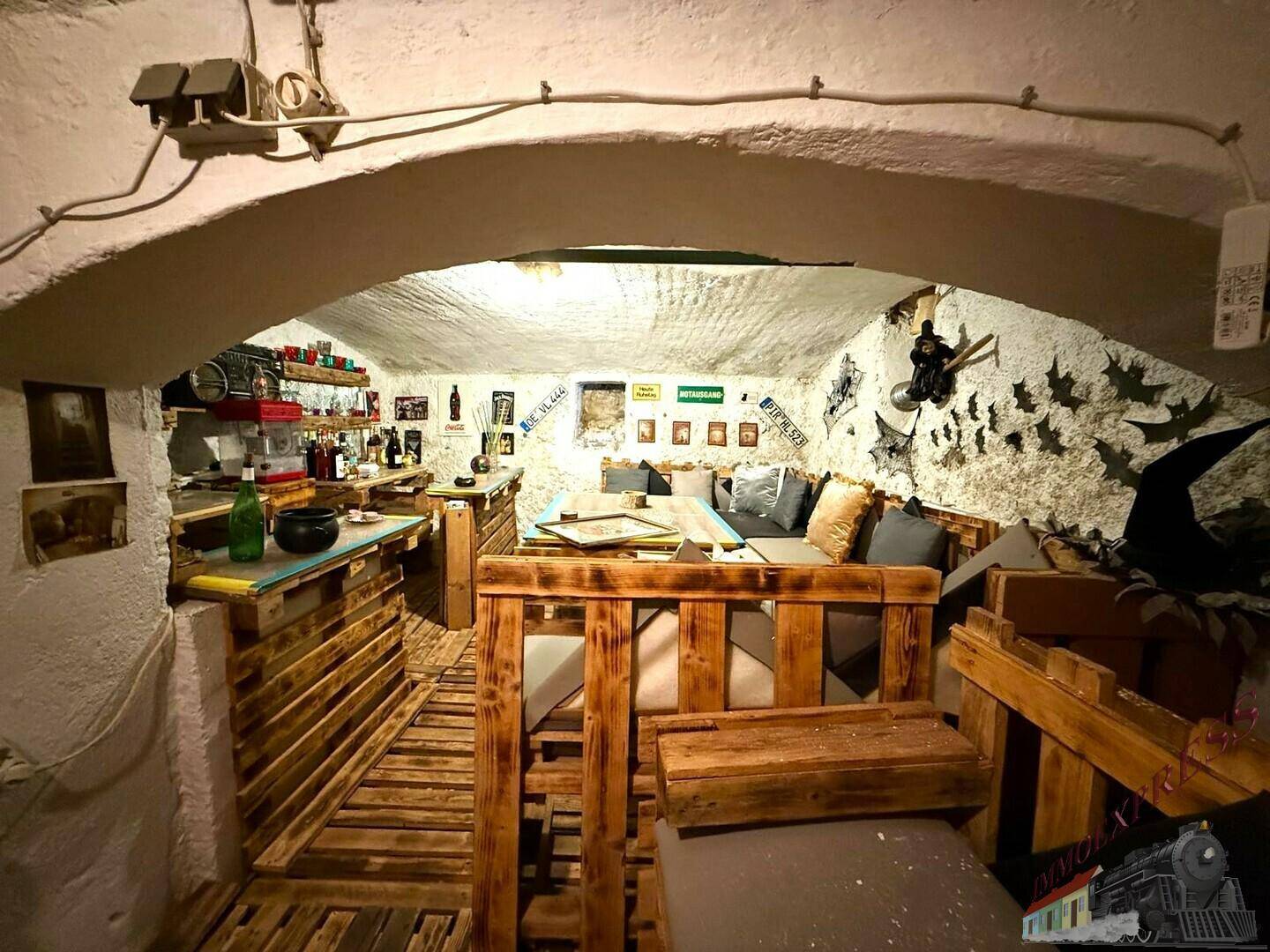 Rustikaler Kellerraum mit niedriger Gewölbedecke und Möbeln aus Paletten, ideal als Bar oder Hobbyraum.