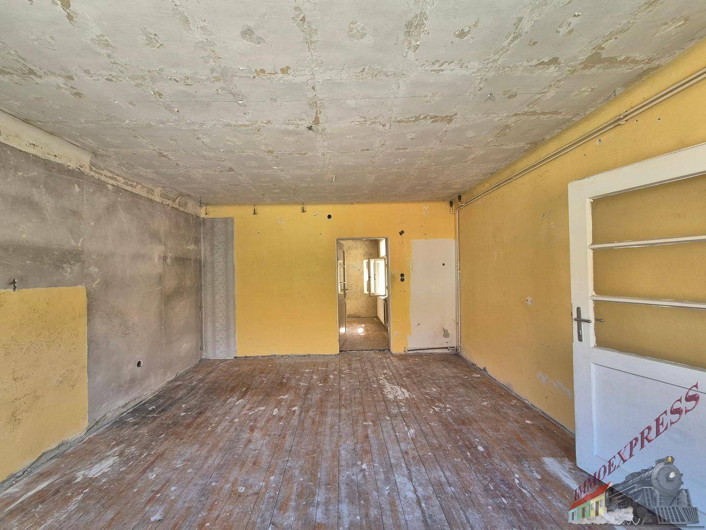 Geräumiges Wohnzimmer in Renovierung mit gelben Wänden und Blick in angrenzende Räume.