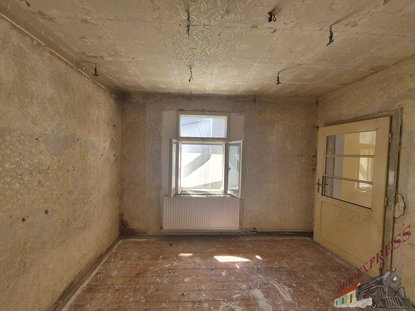 Helles Schlafzimmer mit Fenster und Holzdielenboden, bereit für die Modernisierung.