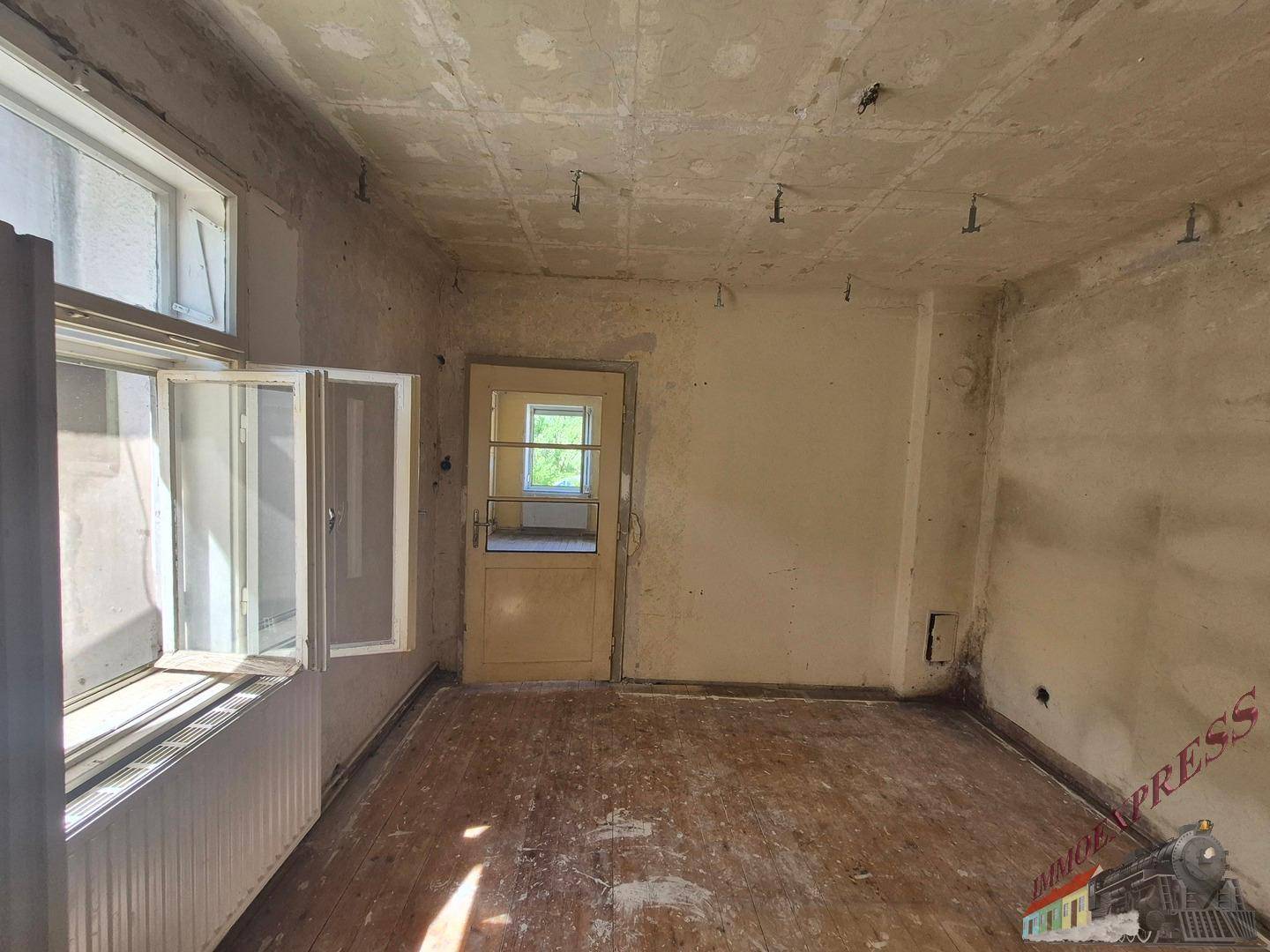 Schlafzimmer in Renovierung mit Holzdielenboden, Fenster und einer Holztür.