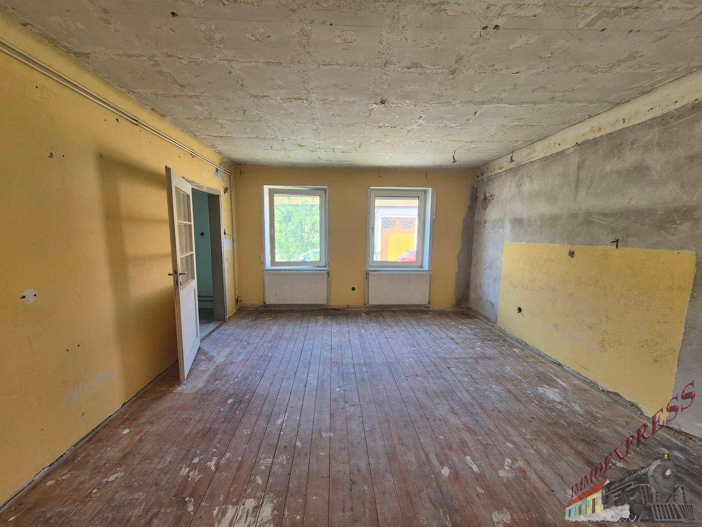 Renovierungsbedürftiges Wohnzimmer mit gelben Wänden und altem Holzdielenboden.