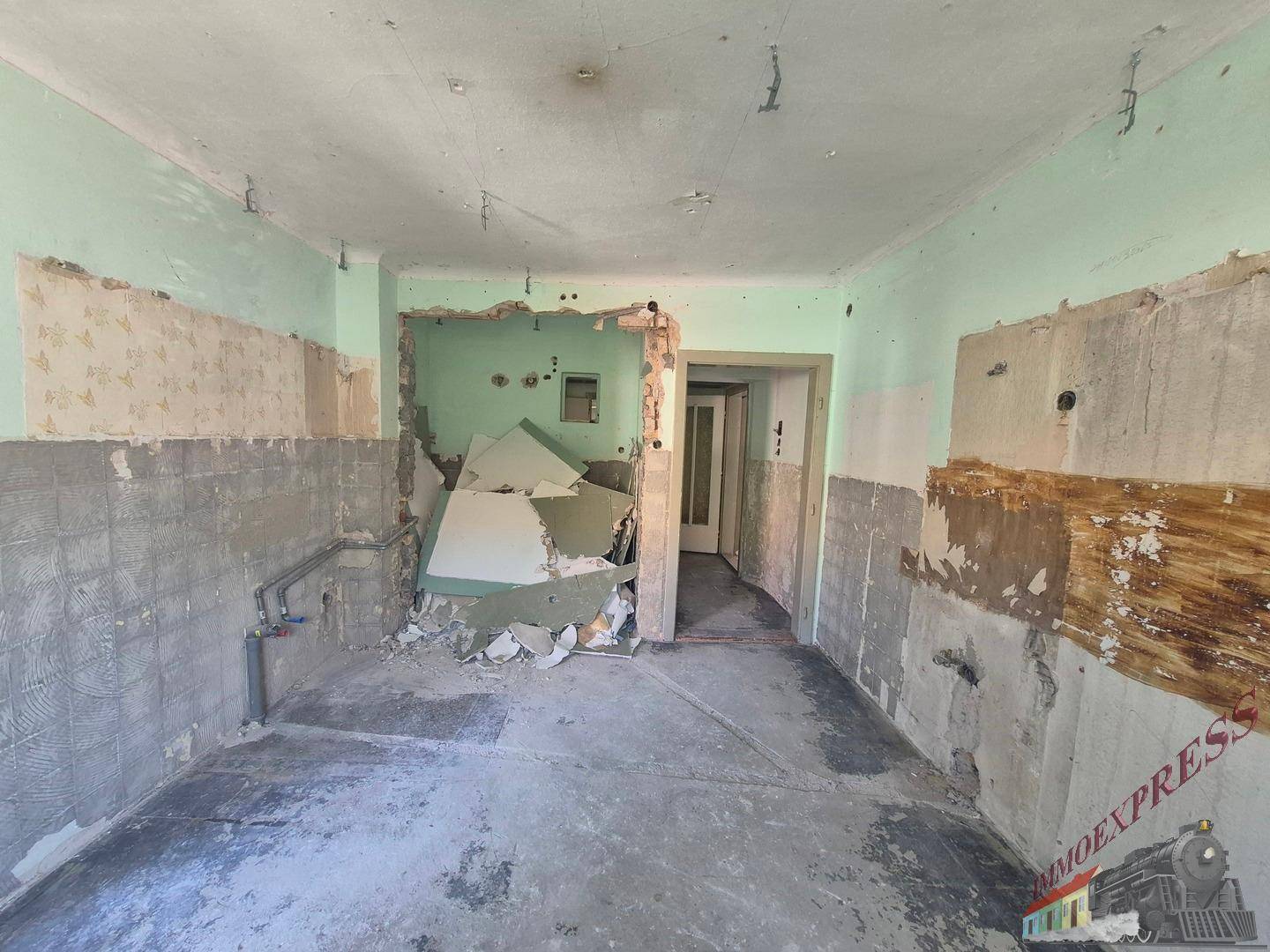 Raum in Abrissphase, vermutlich eine Küche, mit sichtbaren Installationsresten und Bauschutt.