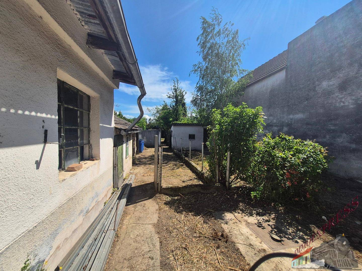 Schmaler Gartenweg entlang der Hauswand mit Blick auf weitere Nebengebäude.