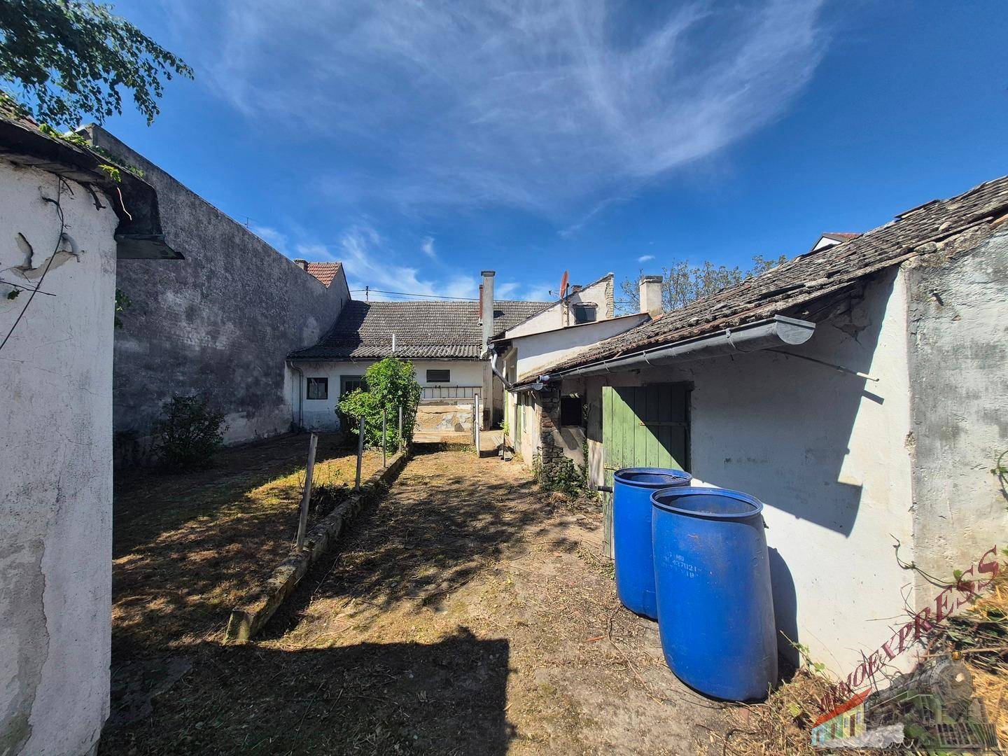 Hinterhofbereich zwischen Gebäuden mit blauen Regentonnen und ungenutzter Grünfläche.