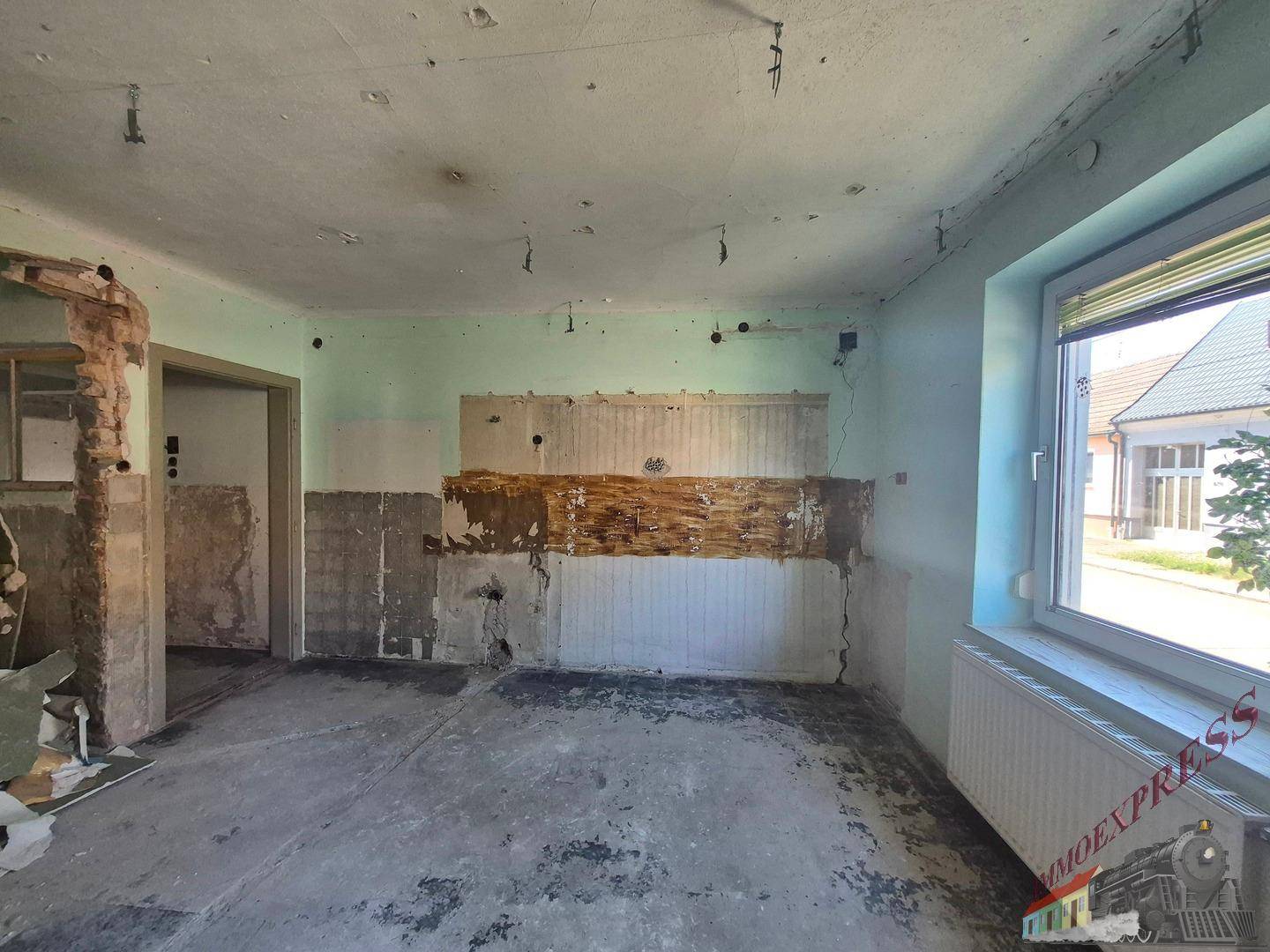 Renovierungsbedürftige Küche mit entfernten Fliesen und Blick auf die Straße durch das Fenster.