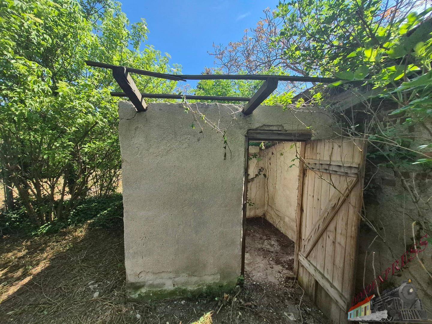 Verfallener Schuppen im Gartenbereich mit offener Holztür und sichtbaren Holzbalken.