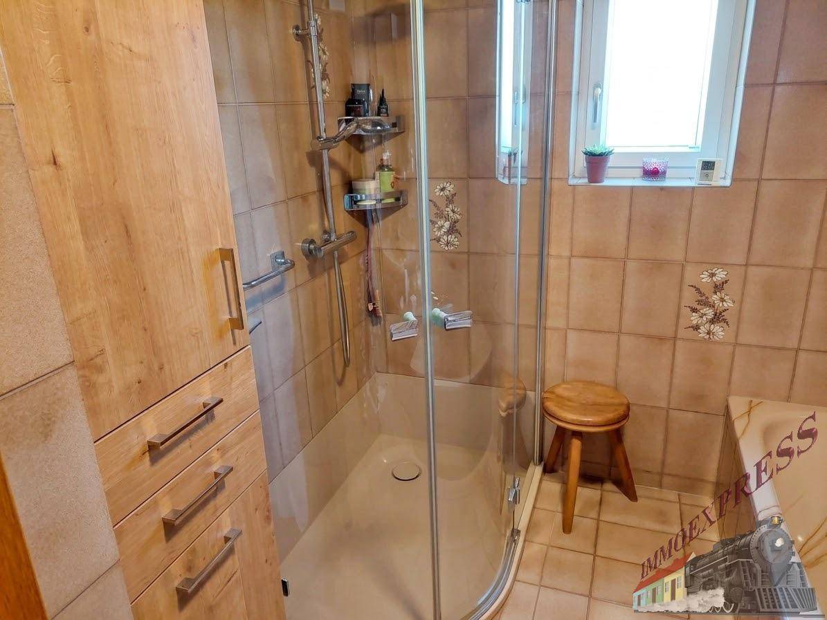 Funktionales Badezimmer mit Duschkabine, Holzschrank und Fenster, gefliest in warmen Brauntönen.
