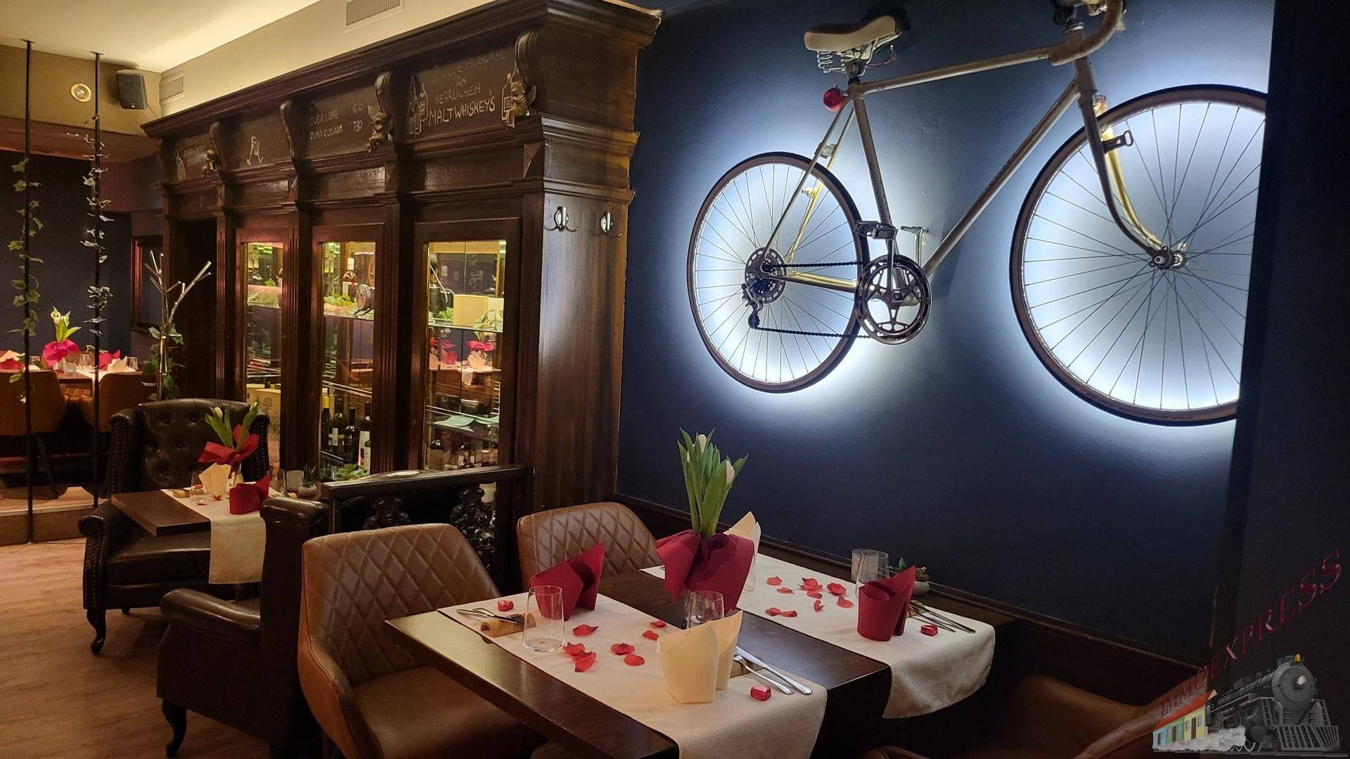 Gemütlicher Restaurantbereich mit dunklem Holzschrank, beleuchtetem Fahrrad und gedeckten Tischen.