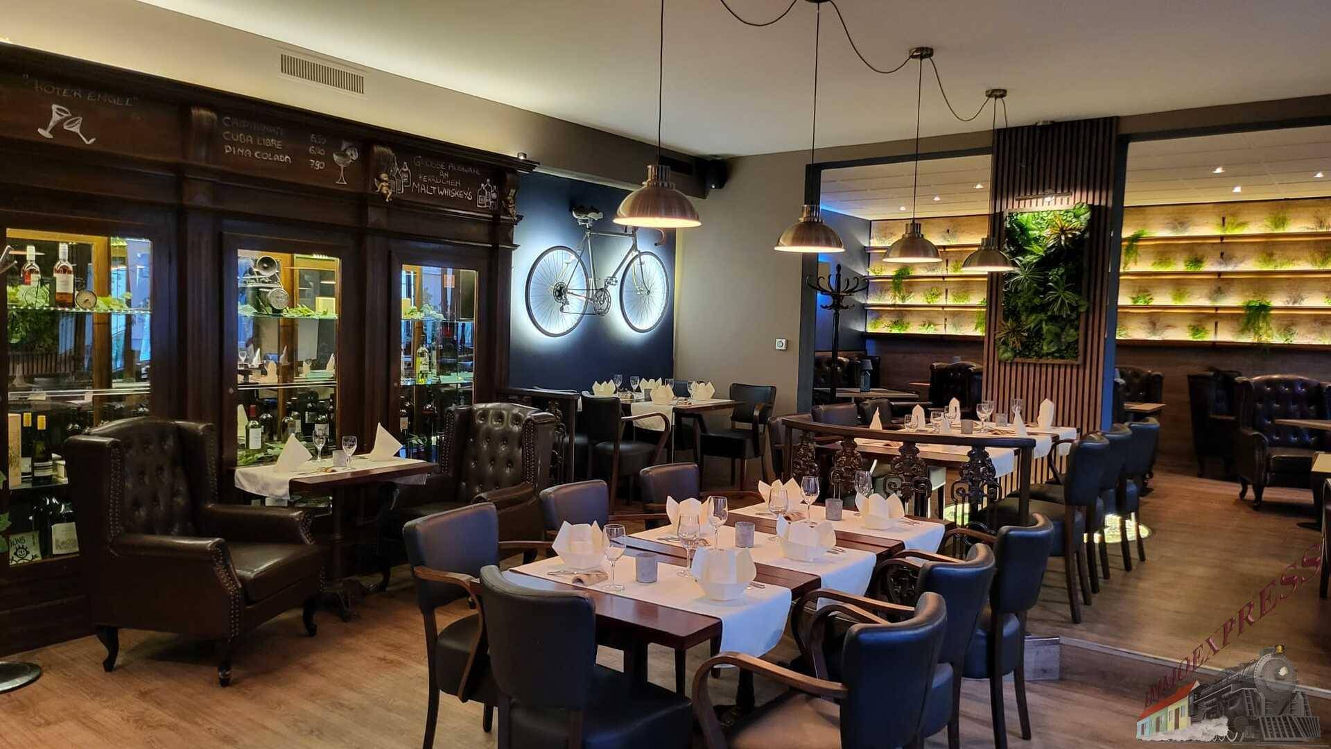Geräumiger Restaurantbereich mit dunklen Holzmöbeln, Ledersesseln und einer beleuchteten Pflanzenwand.