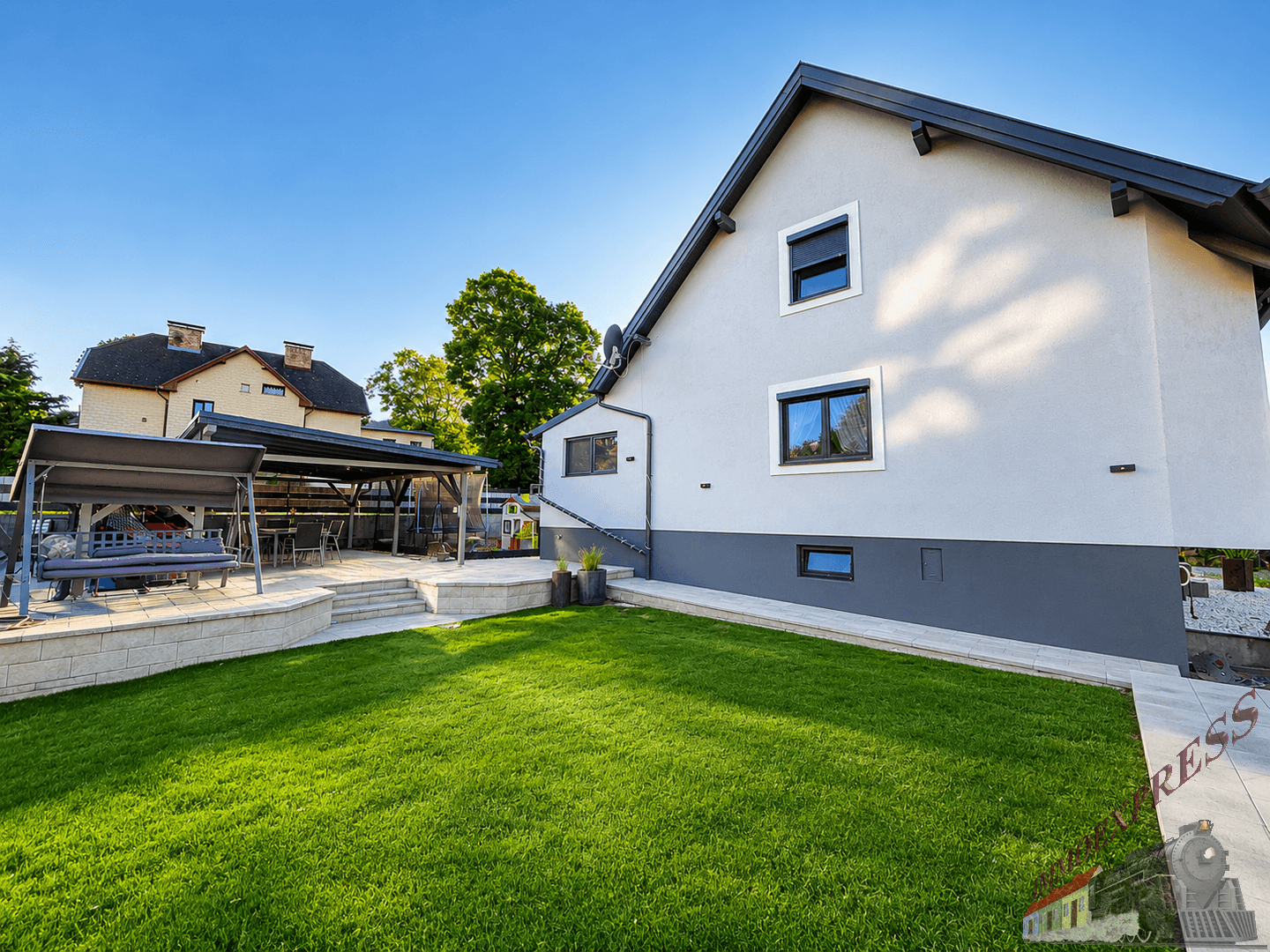 Gepflegter Garten mit Rasenfläche und überdachtem Sitzbereich am Haus.