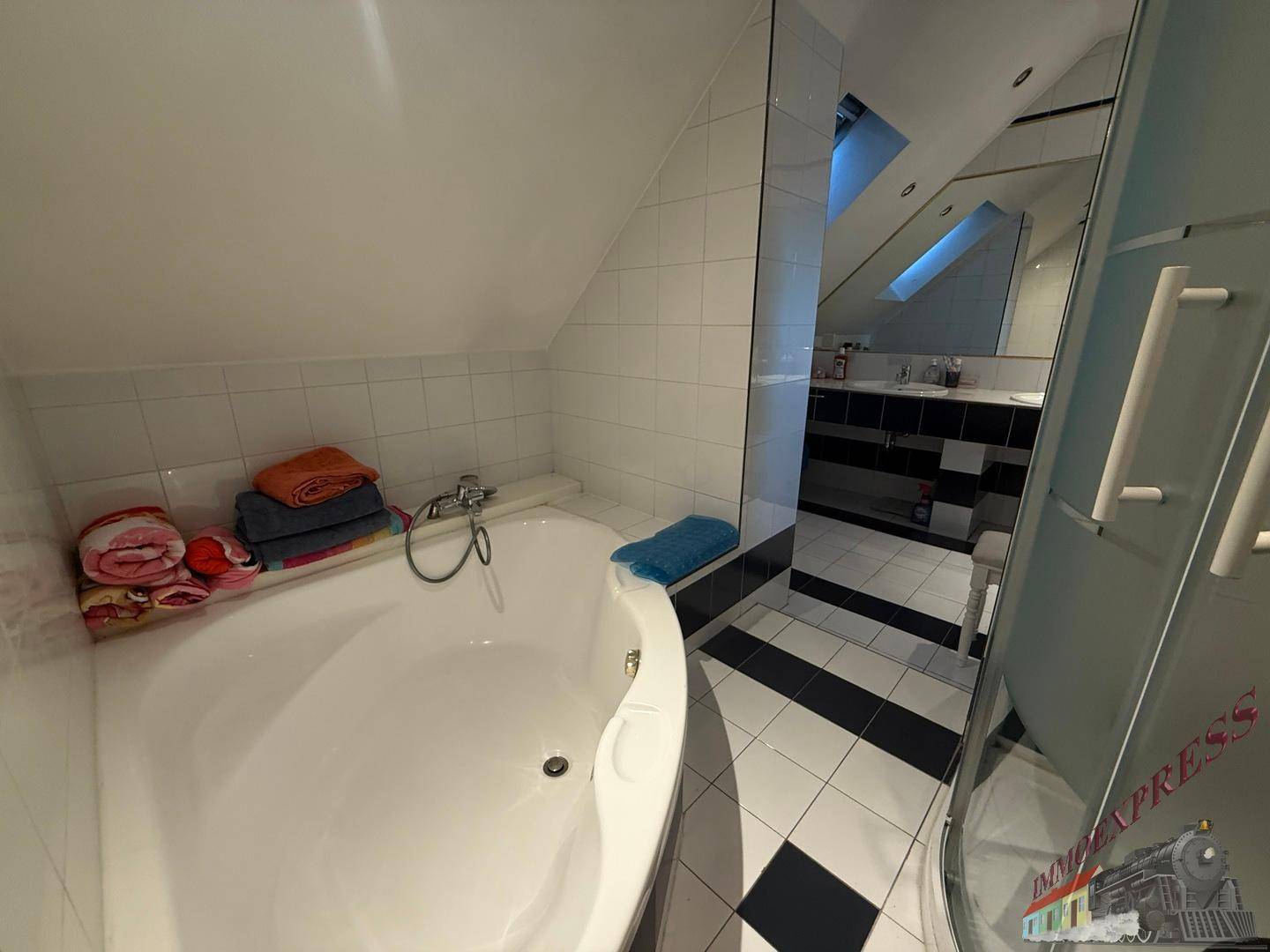Badezimmer im Dachgeschoss mit Badewanne, Duschkabine und schwarz-weißen Fliesen.