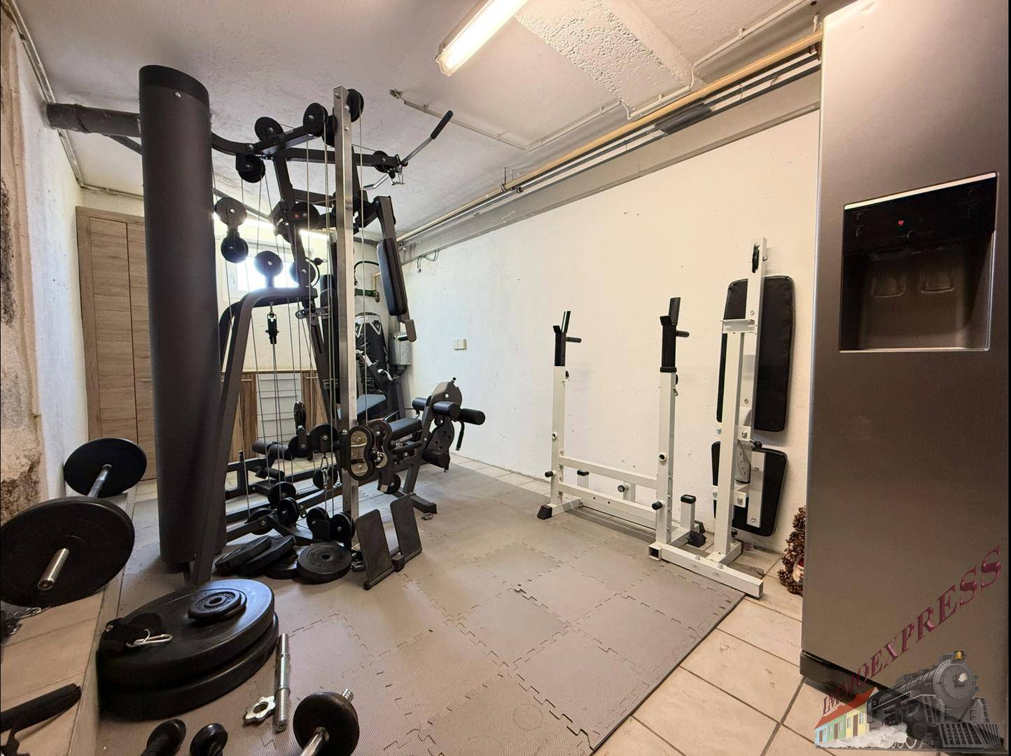 Privater Fitnessraum mit verschiedenen Trainingsgeräten und Fliesenboden.