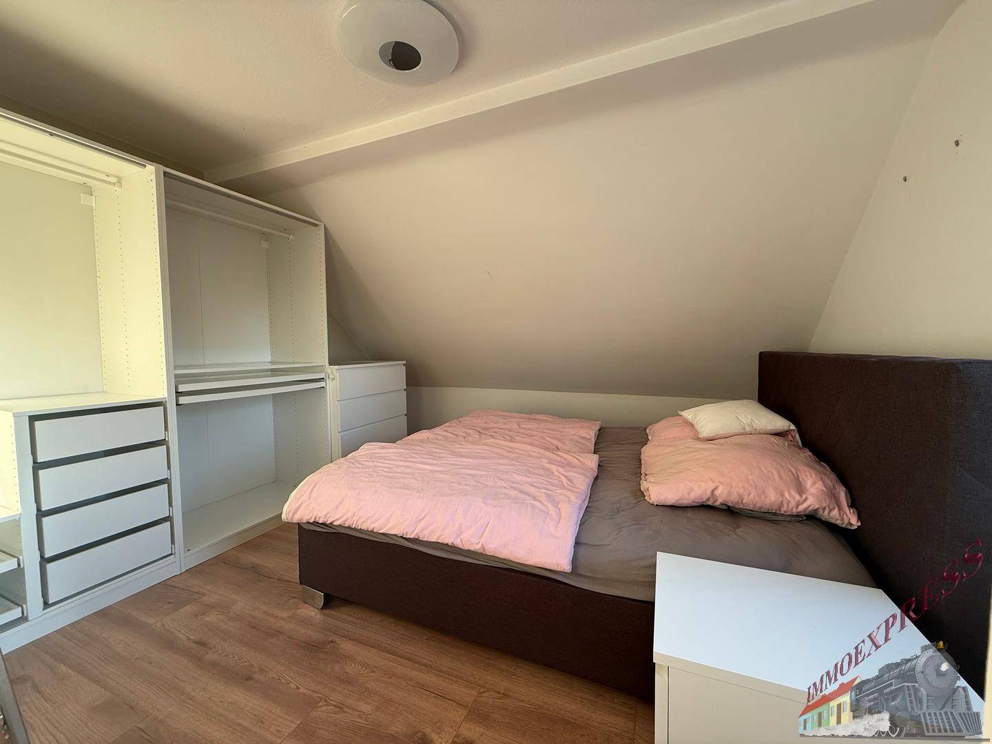 Schlafzimmer im Dachgeschoss mit Bett, Einbauschränken und Laminatboden.