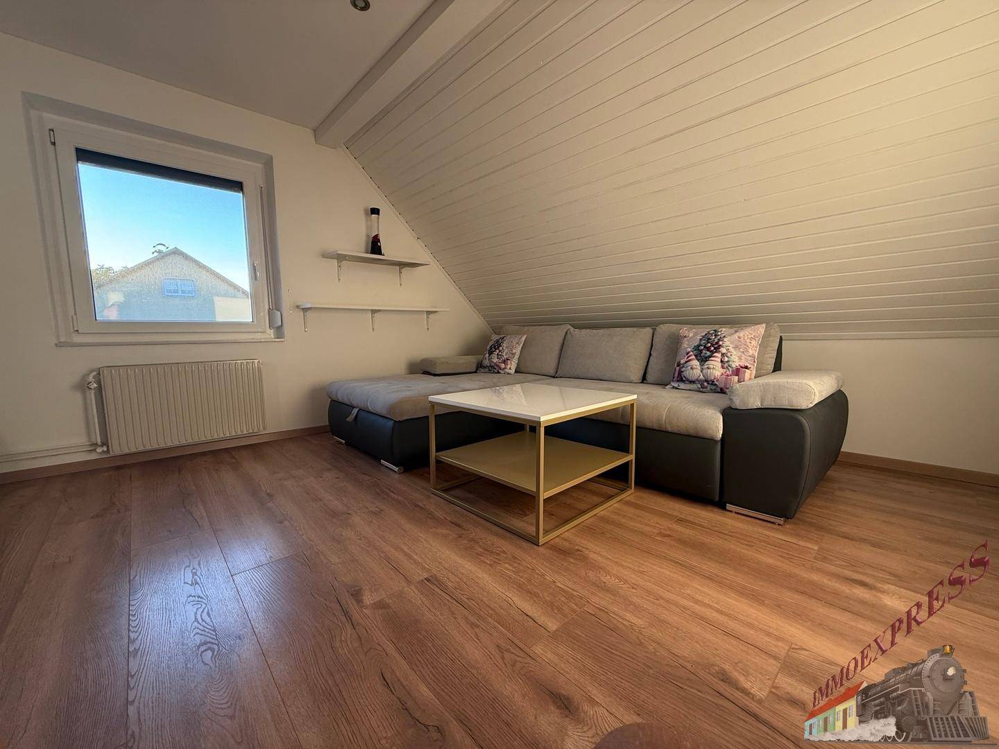 Gemütliches Wohnzimmer im Dachgeschoss mit Sofa und Holzbalkendecke.