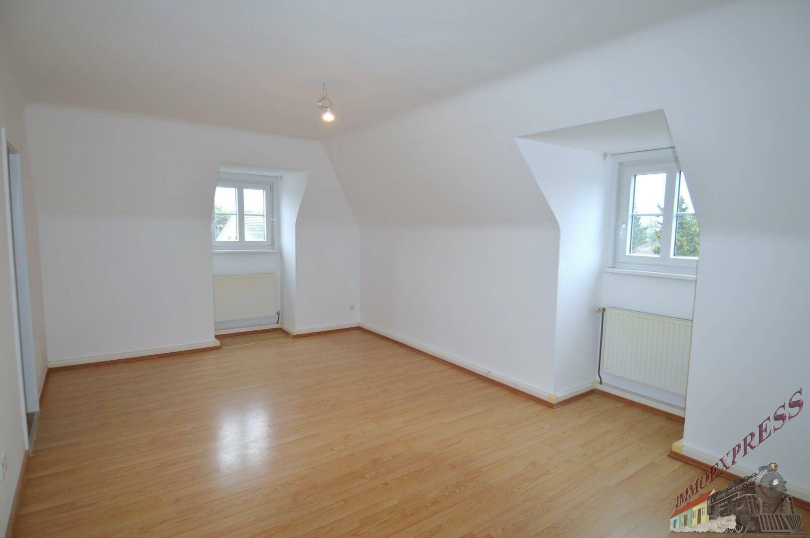 Geräumiges Dachgeschosszimmer mit Laminatboden, schrägen Wänden und zwei Fenstern.
