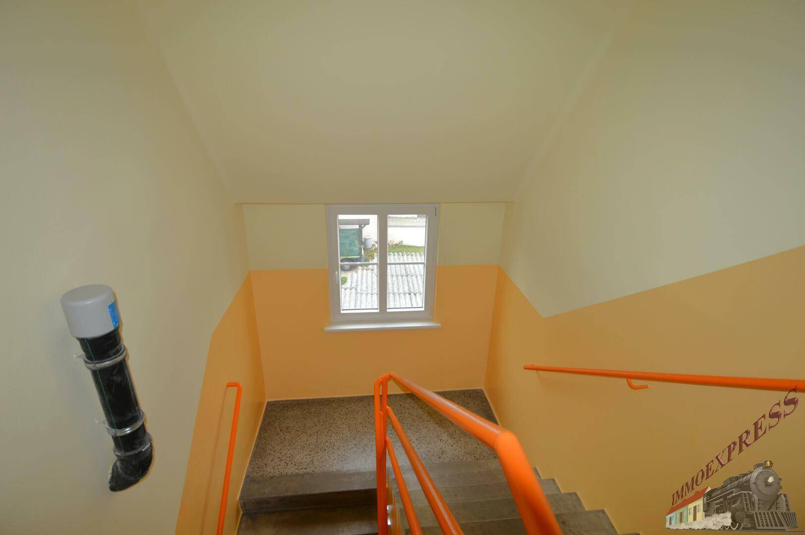 Treppenhaus mit orangefarbenen Handläufen und Fenster für natürliches Licht.
