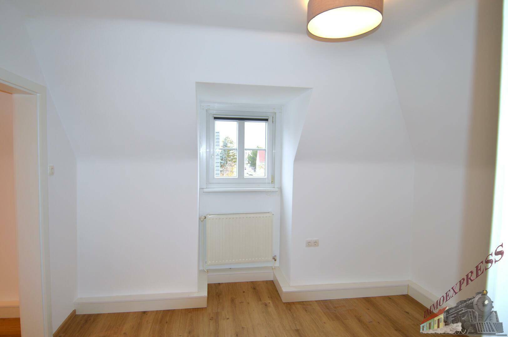 Gemütliches Dachgeschosszimmer mit Laminatboden und Fenster.