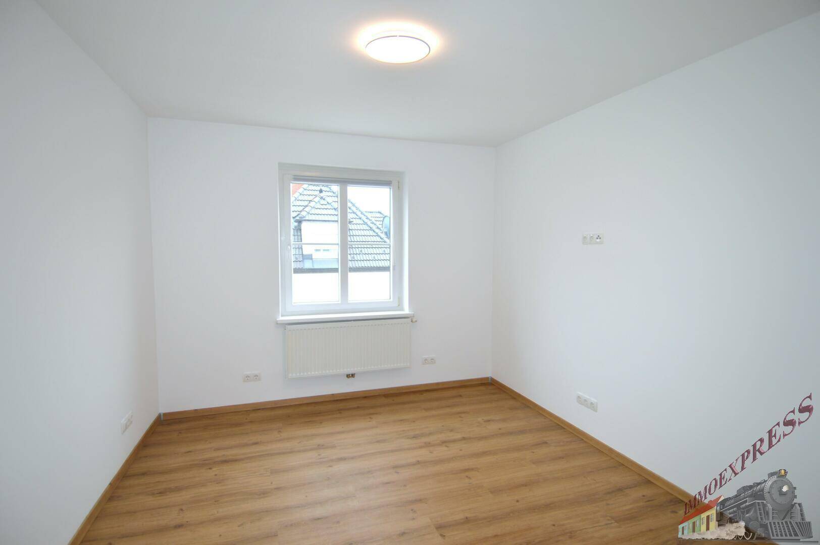 Helles Schlafzimmer mit Laminatboden und einem Fenster mit Blick nach draußen.