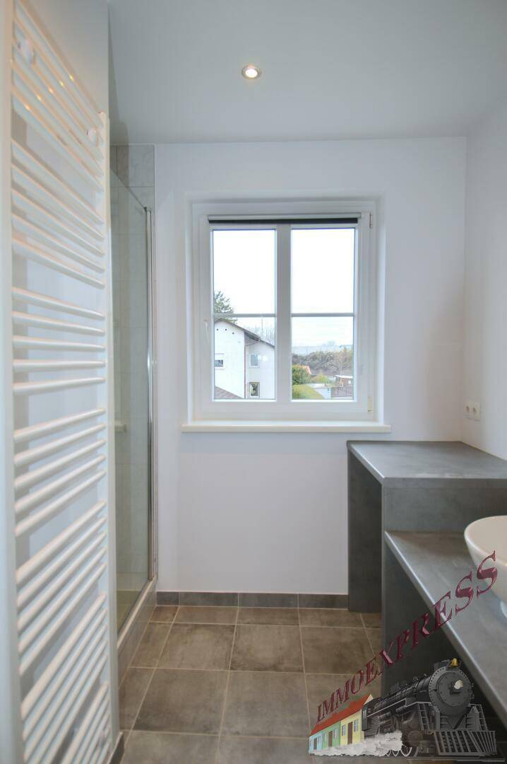 Geräumiges Badezimmer mit Dusche, Fenster und modernem Waschtisch.
