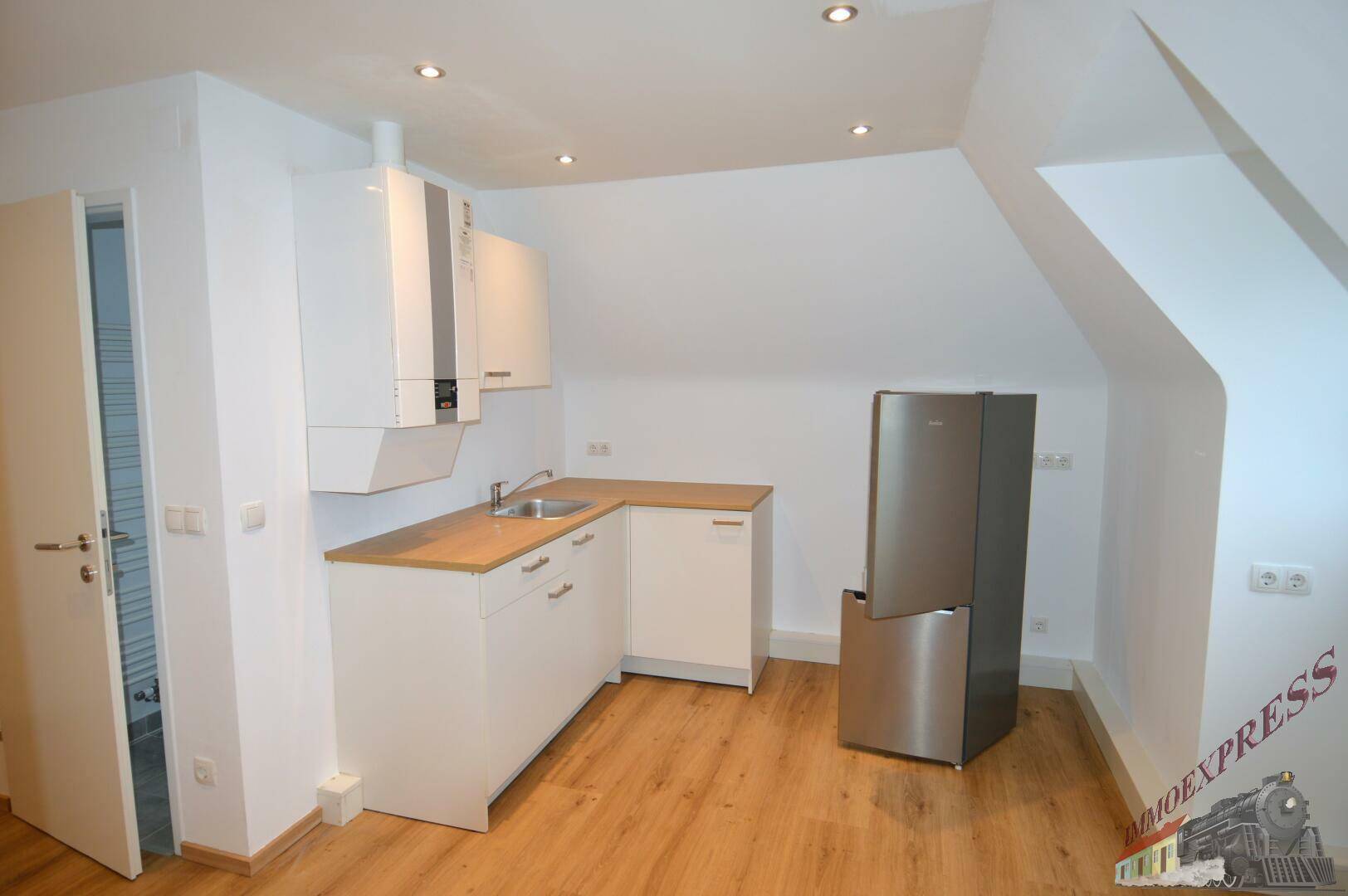 Kompakte Kochnische mit weißen Schränken, Holztheke und freistehendem Kühlschrank im Dachgeschoss.