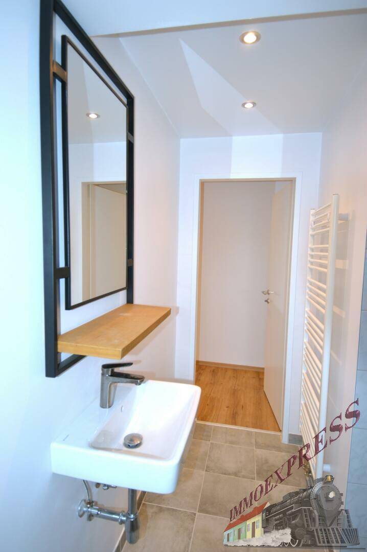 Modernes Badezimmer mit rechteckigem Waschbecken, Holzablage und großem Spiegel mit schwarzem Rahmen.