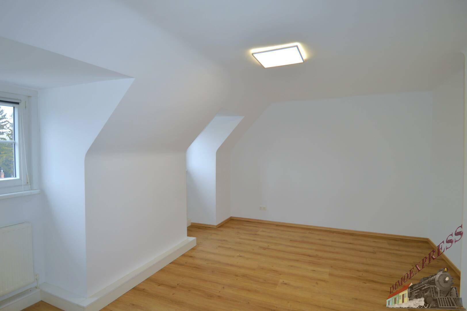 Geräumiges Dachzimmer mit schrägen Wänden, Laminatboden und Fenster.