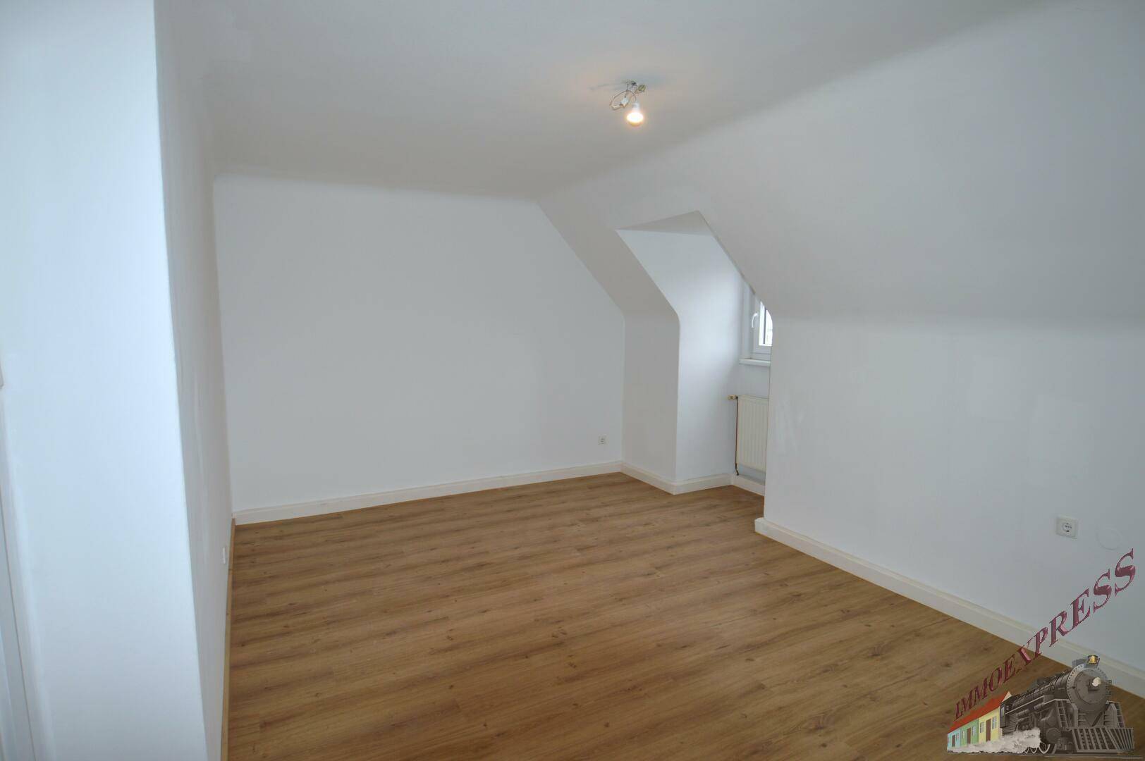 Dachzimmer mit schrägen Wänden, Laminatboden und einem Fenster.
