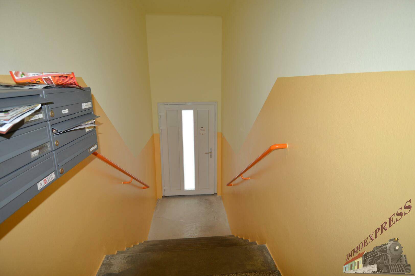 Treppenhaus mit gelb-orangen Wänden, Briefkästen und Handläufen.