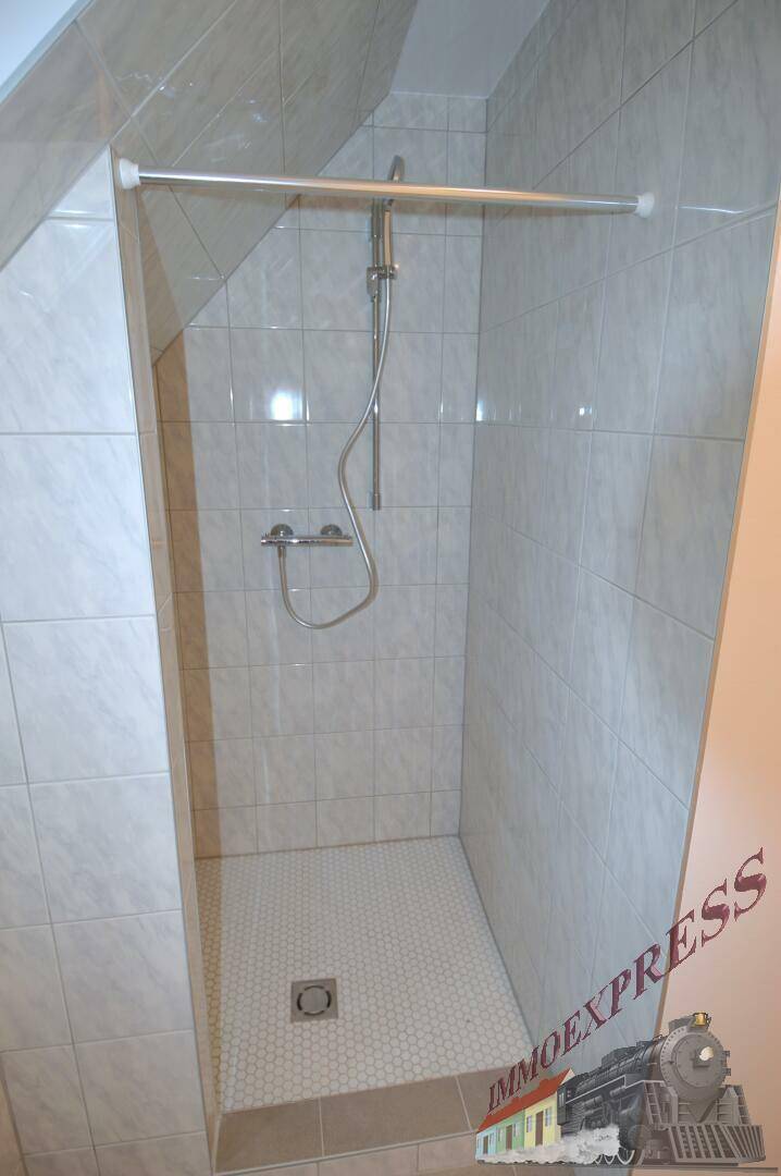 Duschbereich im Badezimmer mit hellen Fliesen und Mosaikboden.