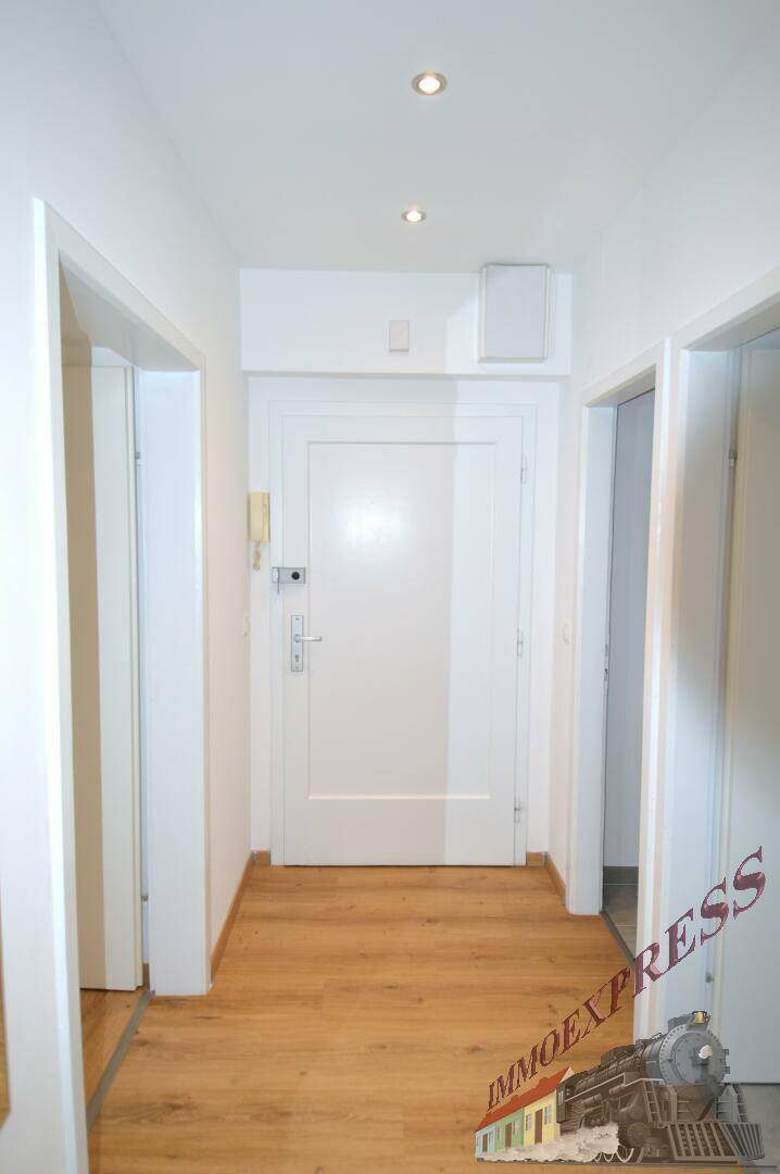 Heller Flur mit Laminatboden, weißer Eingangstür und Deckenstrahlern.
