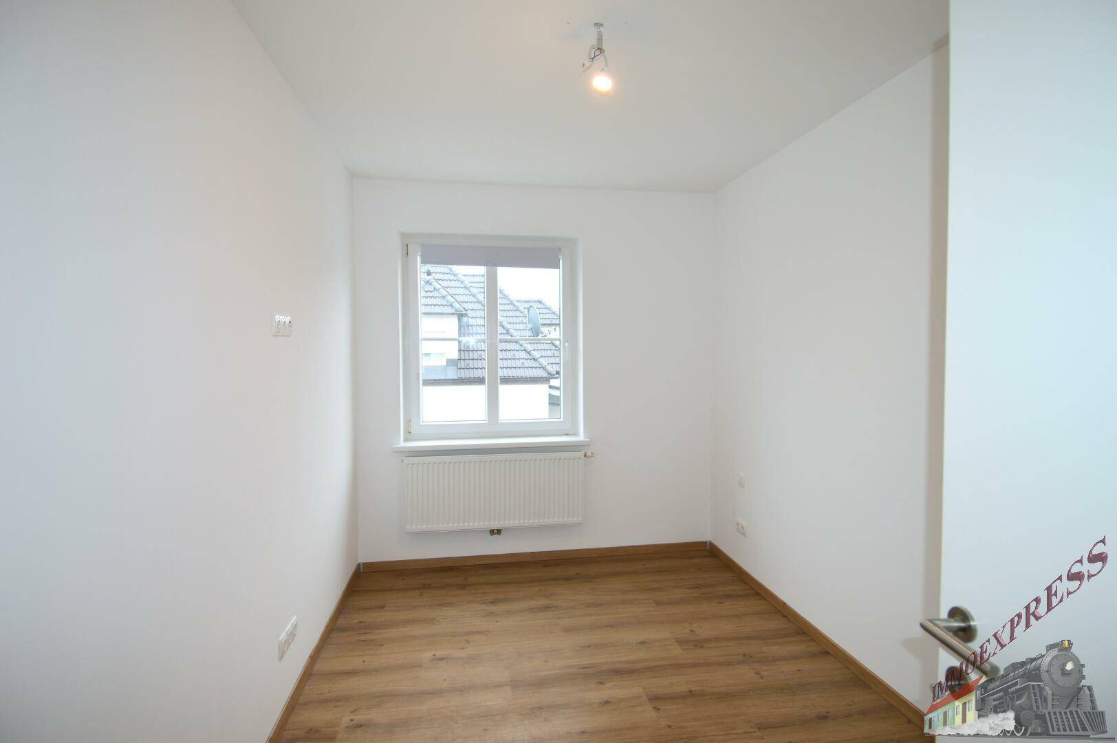 Helles Zimmer mit Laminatboden, weiß gestrichenen Wänden und einem Fenster.
