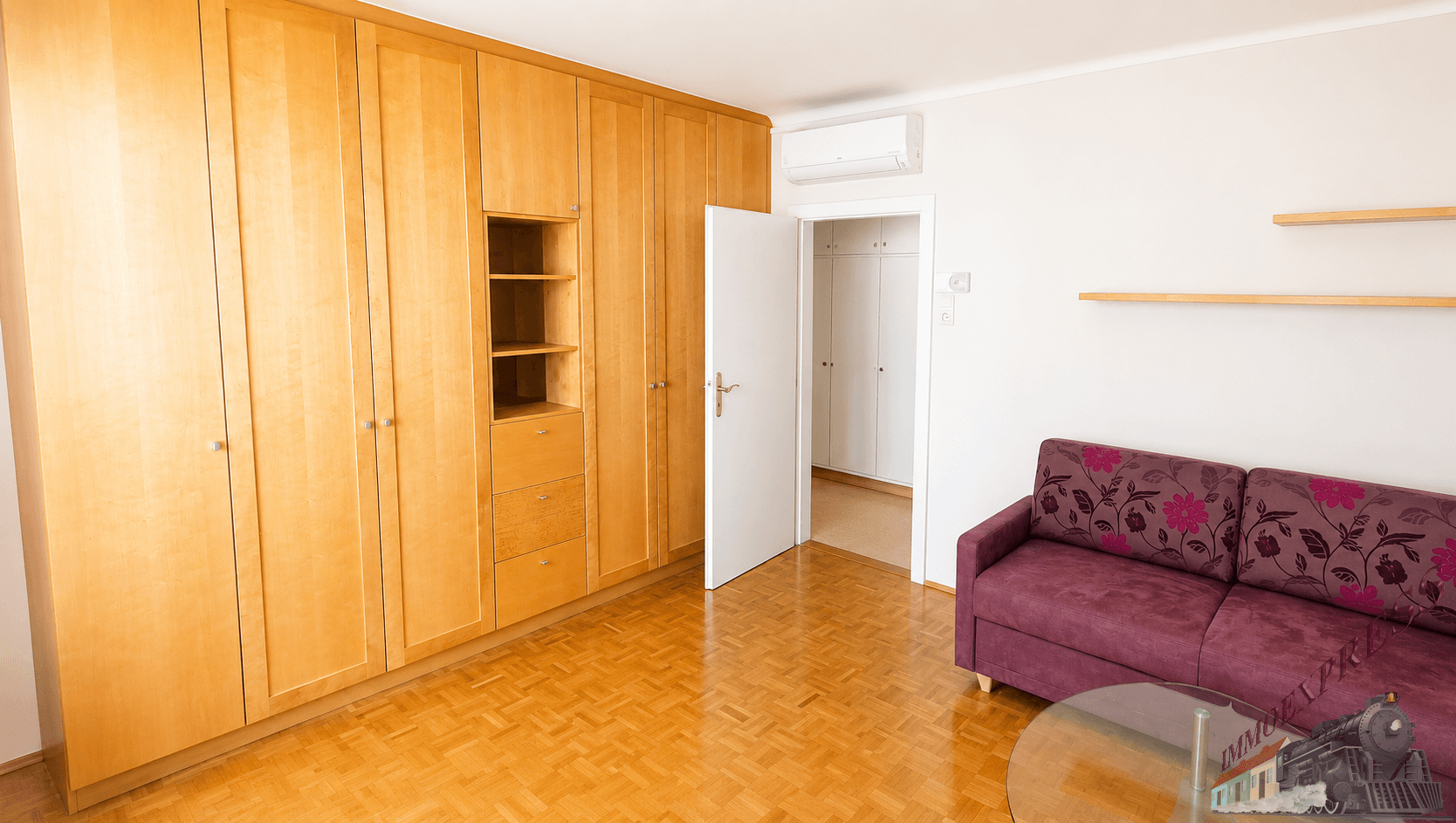 Wohnbereich mit großem Einbauschrank, Sofa und Zugang zu einem weiteren Raum.